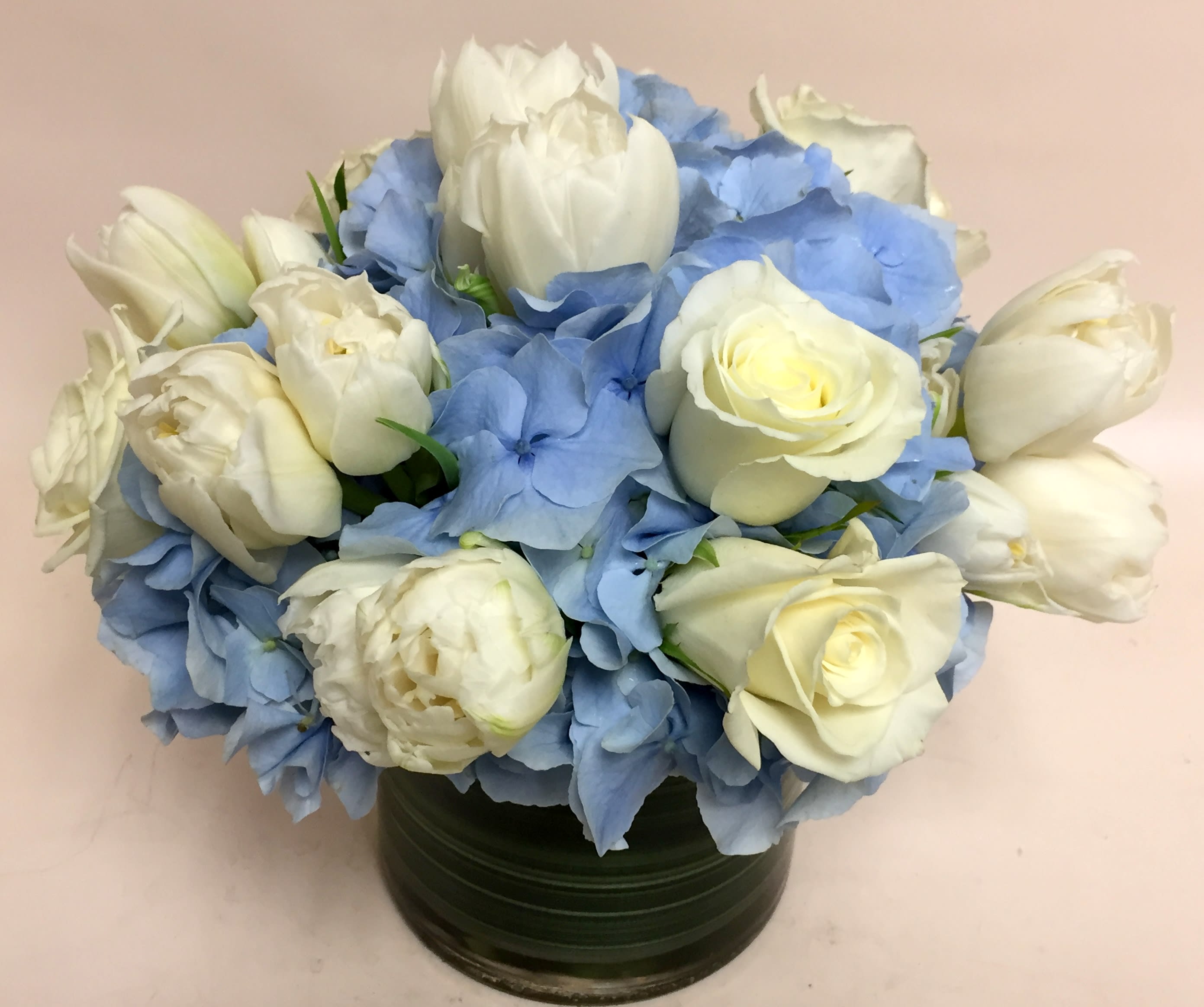 White roses and blue hydrangeas arranged in a dark green vase