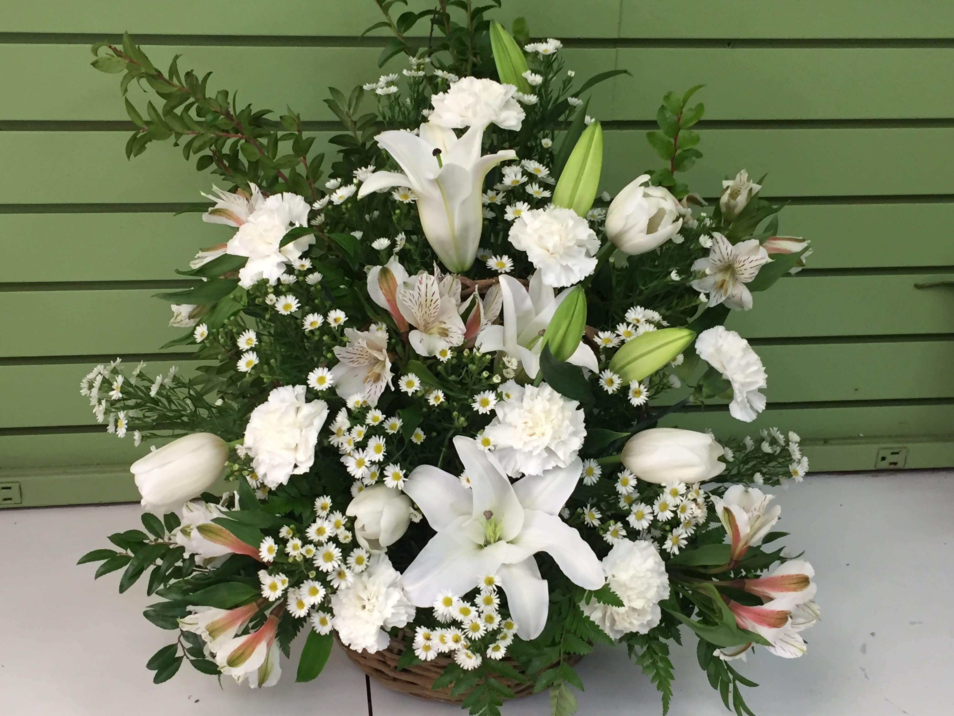 White lilies, carnations, and small daisy flowers arranged in a basket