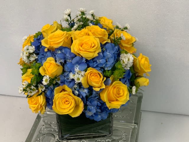 Yellow roses and blue hydrangeas in a square glass vase