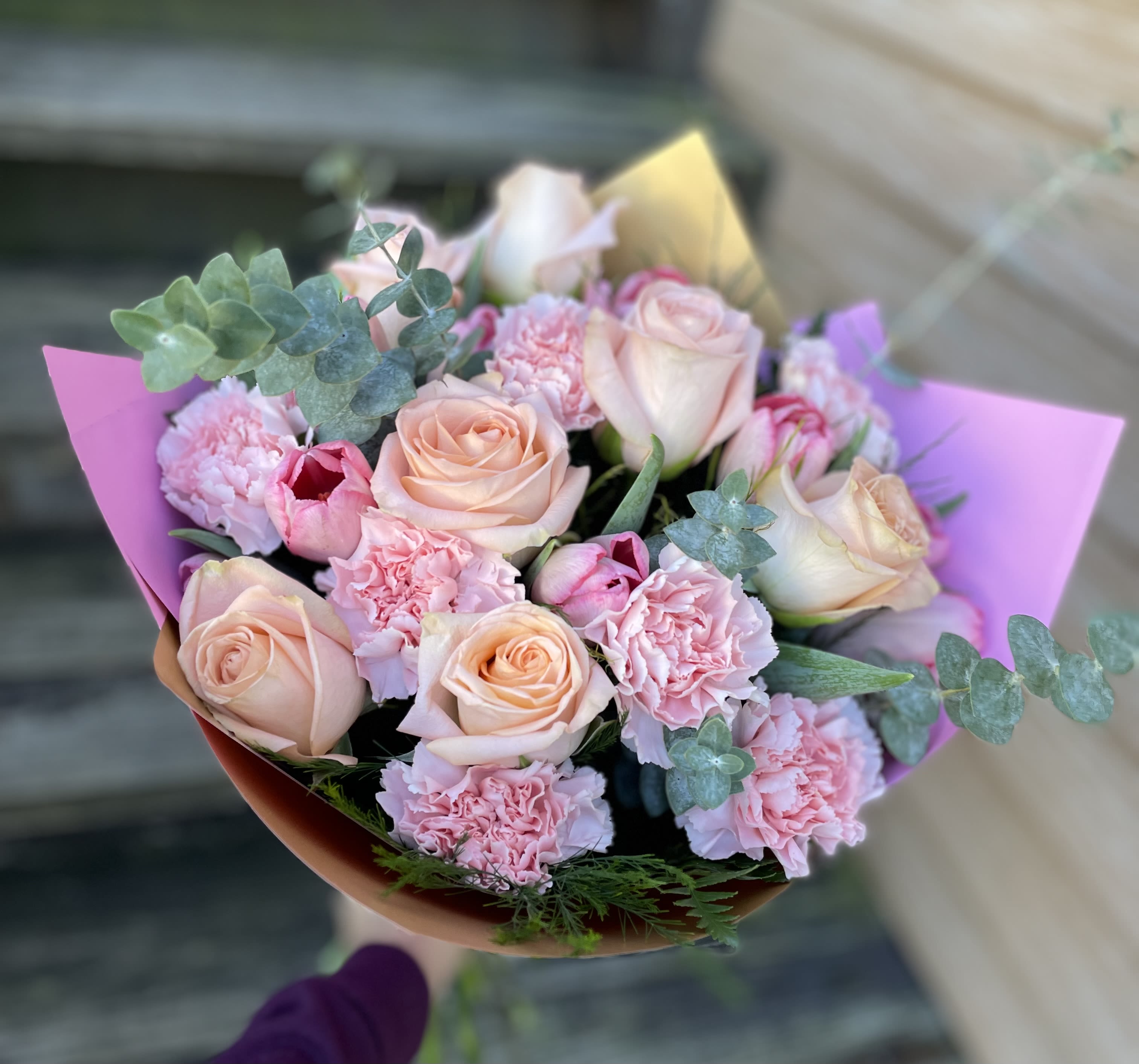 You Are Amazing Bouquet  - Pale peach roses paired with ruffled pink carnations make this You Are Amazing bouquet a gentle, romantic choice for a birthday, thank-you, or just-because surprise. The phrase "flower arrangement" and the everyday gifting use are woven into its soft, feminine personality so the person you're thinking of will feel truly seen and celebrated the moment they unwrap it.  This medium-sized, rounded hand-tied arrangement layers peach roses and pink carnations with silvery eucalyptus for a cool, airy texture. Soft purple and pink wrapping paper frames the blooms and gives the bouquet a delicate, gift-ready finish; the compact, full gathered shape holds together beautifully in the bouquet wrap for easy carrying and display.  