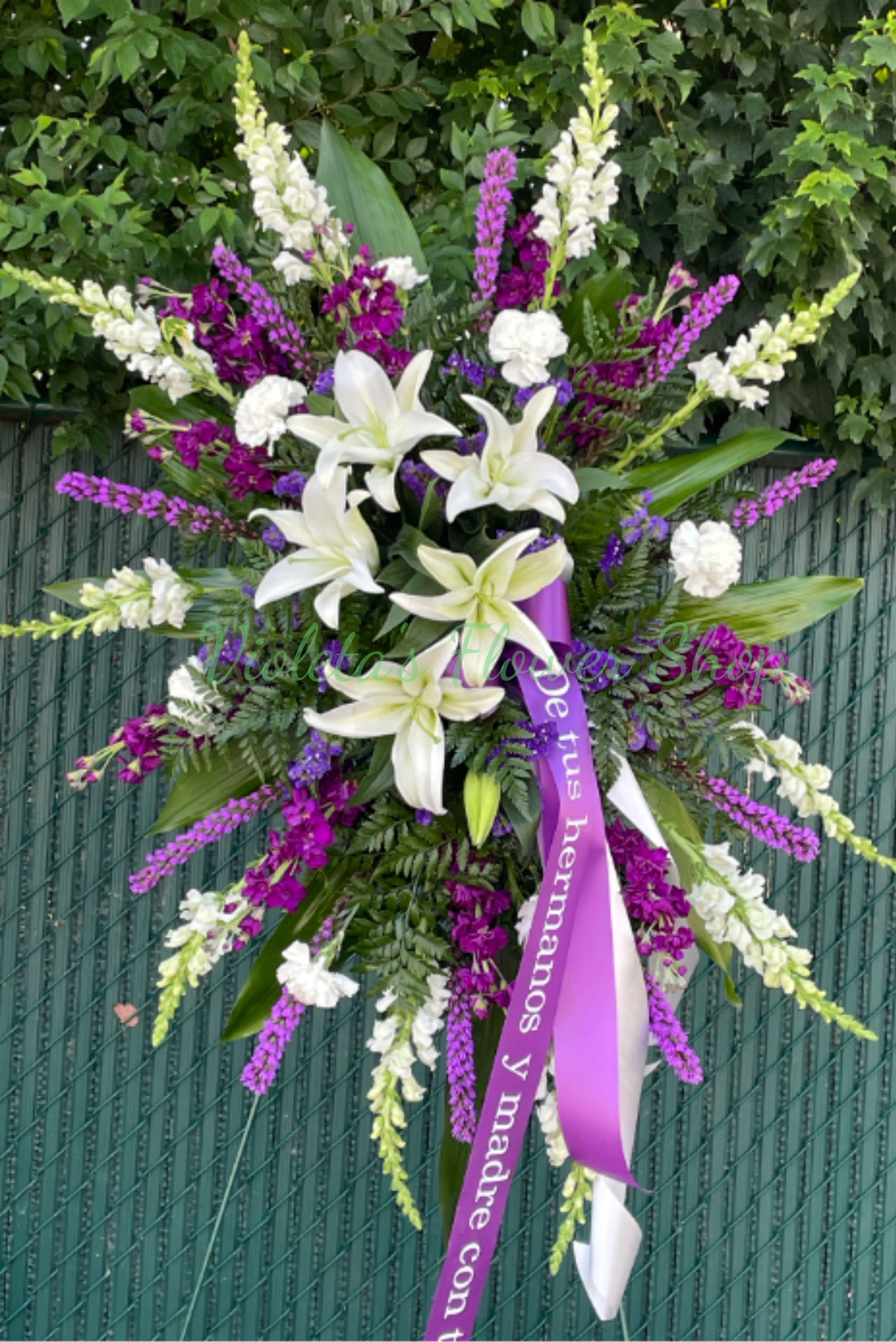 Sympathy Expression Standing Spray - White lilies take center stage in this Sympathy Expression standing spray, making an immediate, comforting impression for a funeral or memorial service. The tall, formal standing spray is designed for sympathy use and reads as a respectful tribute-the white lilies framed by vivid purple and soft pink accents convey dignity, remembrance, and gentle warmth for the person you're honoring. This spray suits a graveside service, chapel display, or a formal memorial where you want the recipient's family to feel seen and comforted. It's built to stand tall and be seen from a distance; no special care is needed on-site beyond placement in a standard easel. If you'd like a custom ribbon message or coordinating sympathy pieces, we can help arrange matching selections.