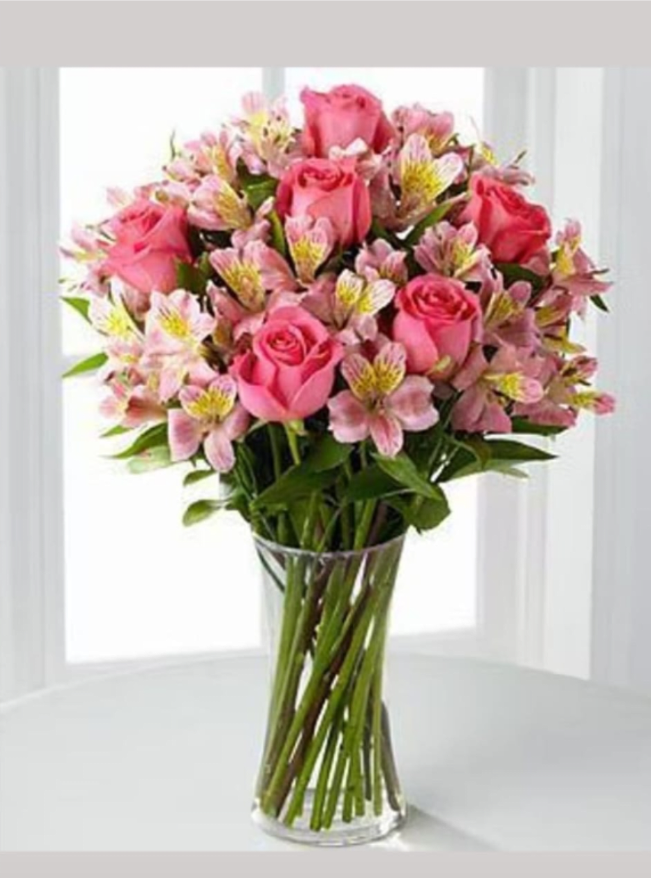 ROCIO - A rounded cluster of soft pink roses and pink alstroemeria makes a gentle, romantic birthday bouquet that also works beautifully for anniversaries, Mother's Day, or a thoughtful just-because gift. The color story-warm pink petals, pale yellow alstroemeria centers, and fresh green foliage-creates a cheerful, uplifting impression that will make the person you're thinking of feel cared for and seen.  Arranged in a clear glass vase, the design shows the long stems for a clean, upright silhouette and a classic table-ready presence. The mix of velvety roses and delicate, freckled alstroemeria petals gives pleasing texture and fullness without fussy extras; the palette reads soft and bright at once, perfect for springtime or any day that needs a gentle lift.  This bouquet is ideal for someone who enjoys traditional florals with a modern, understated look-moms, partners, or friends celebrating a milestone or simply needing a smile. Vase included; keep in fresh water, recut stems if possible, and place away from direct heat to extend bloom life.