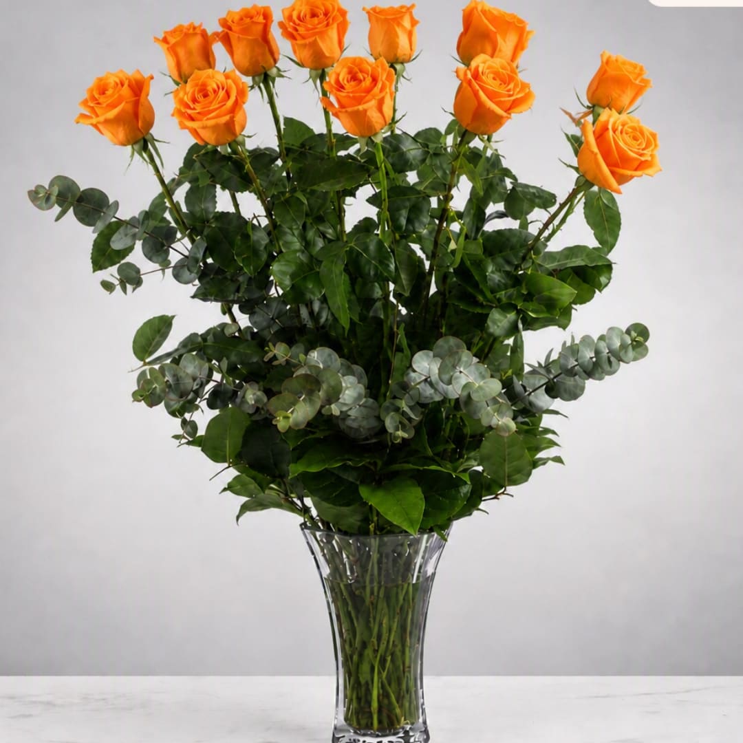 Orange roses arranged in a clear glass vase with mixed greenery