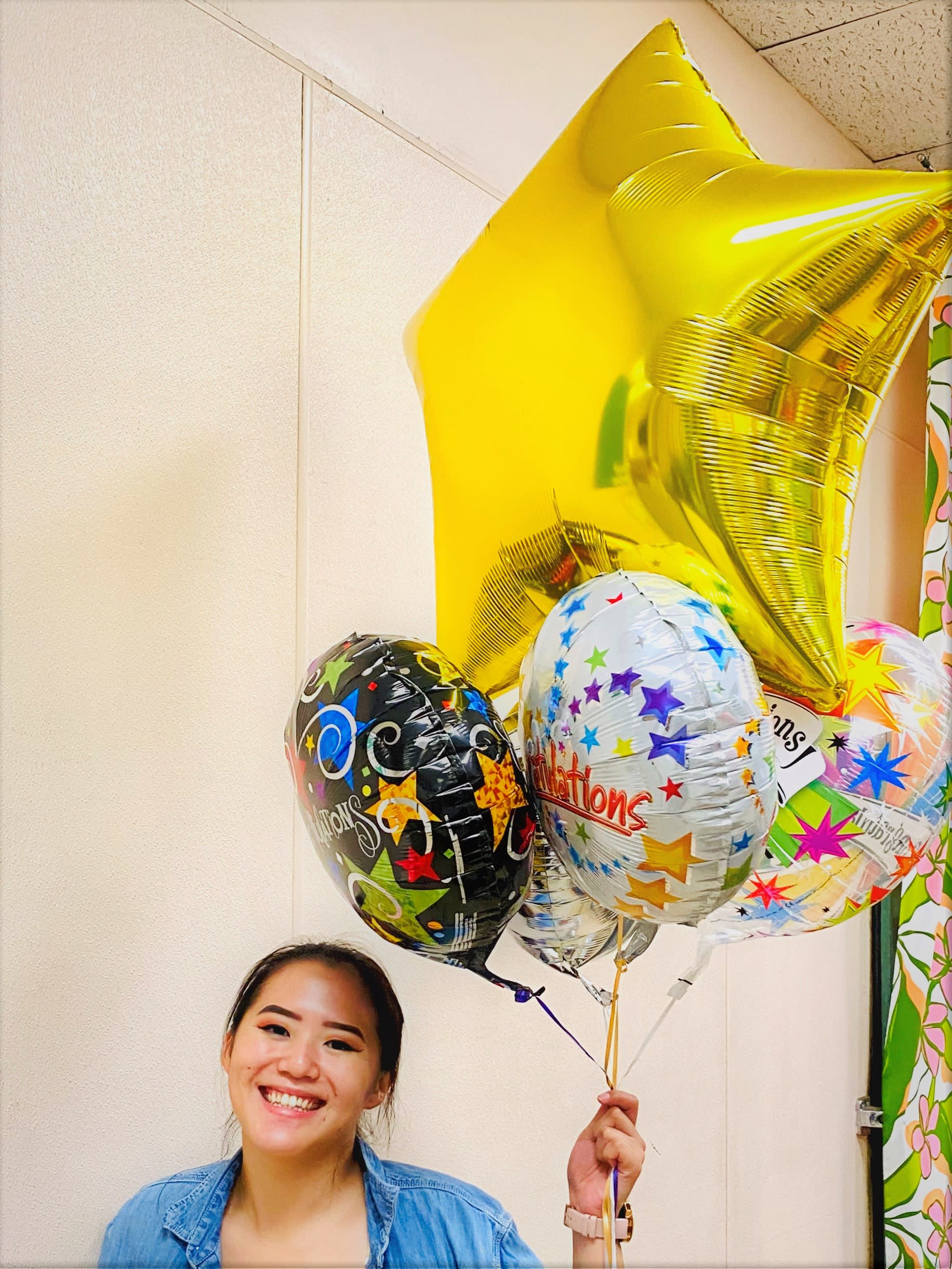 Person smiling and holding a bunch of colorful congratulatory mylar balloons including a large gold star.