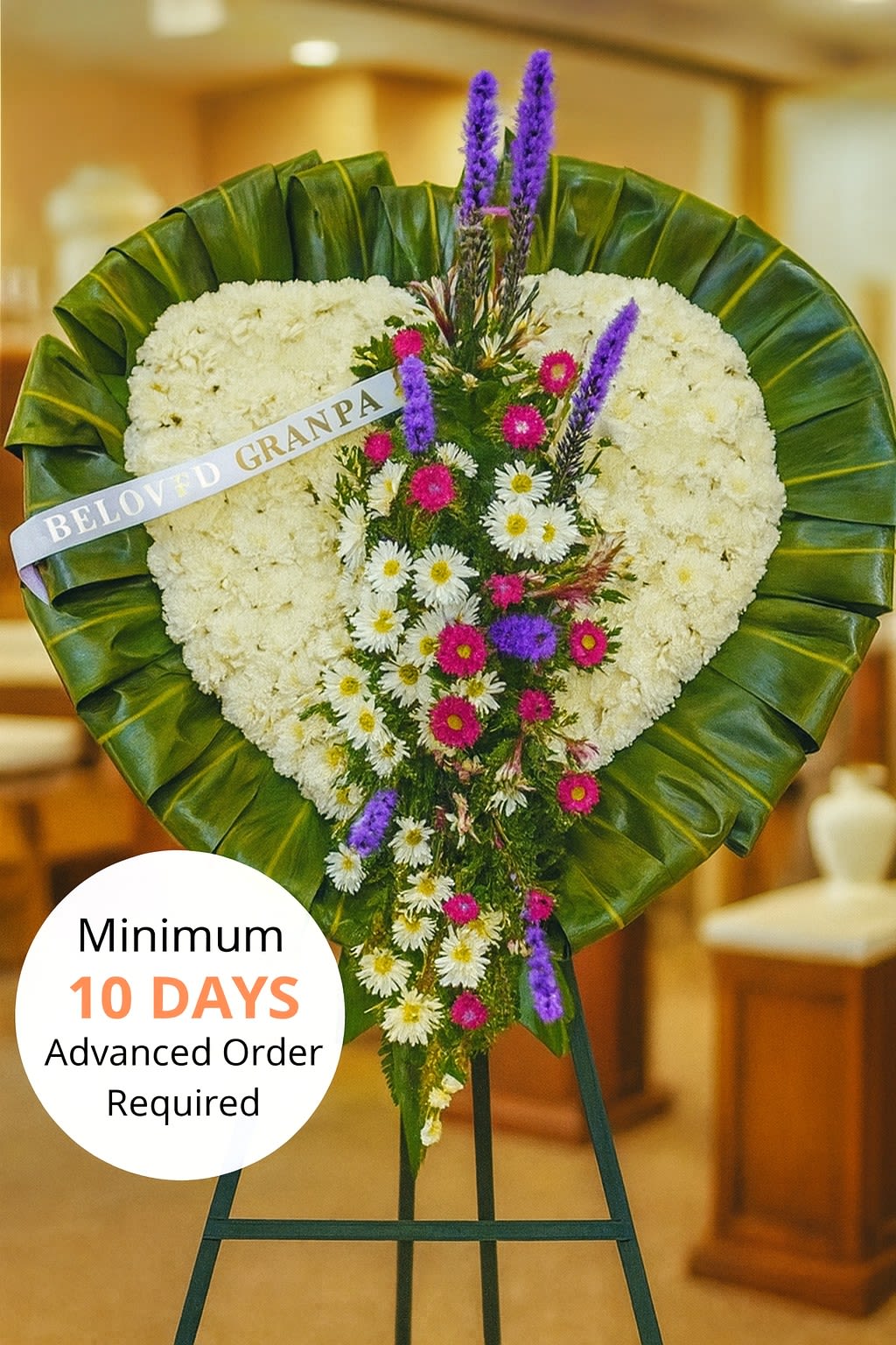 Heart-shaped white sympathy standing spray with cascading purple and pink flowers on a green-leaf border