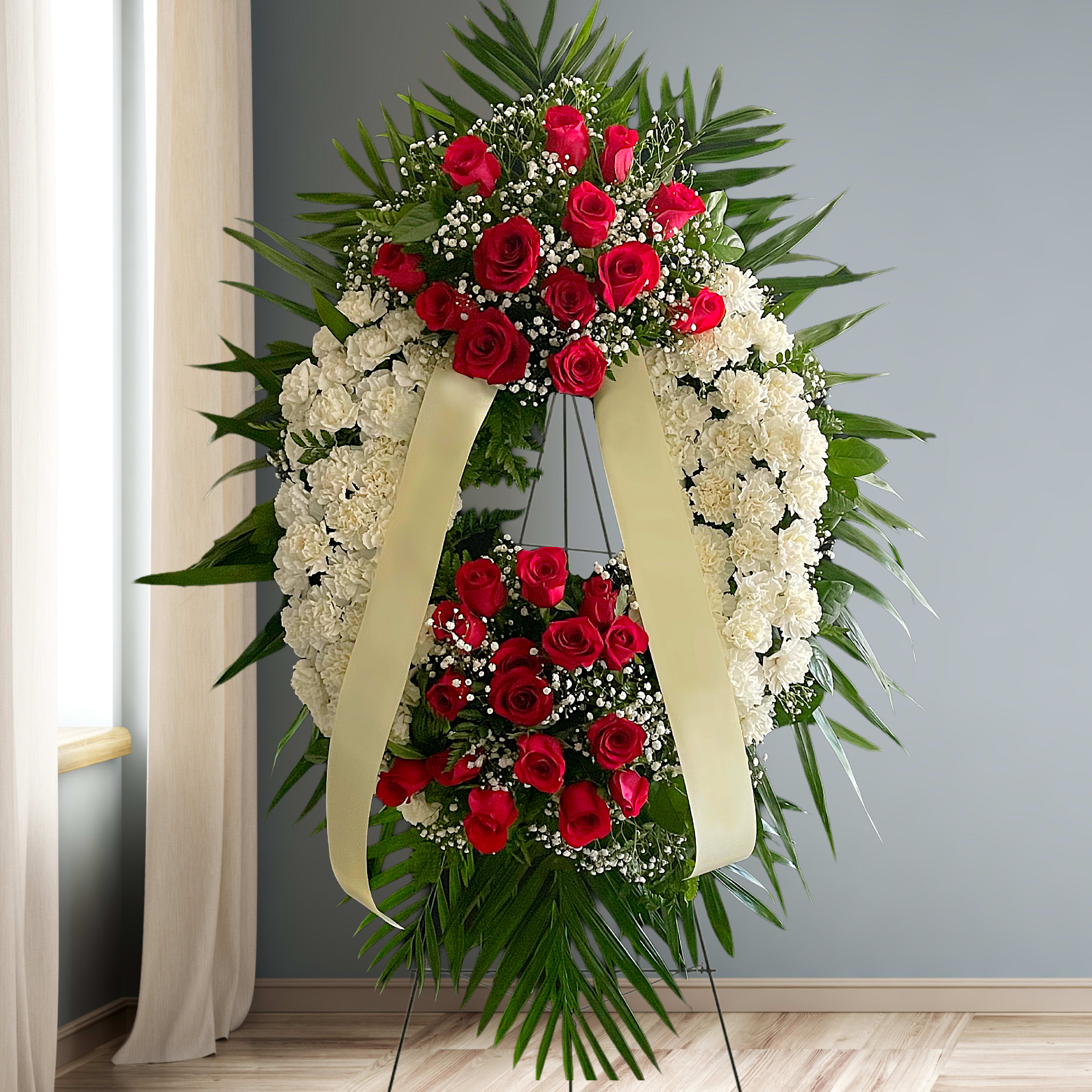Standing funeral wreath of red roses and white carnations with cream ribbons