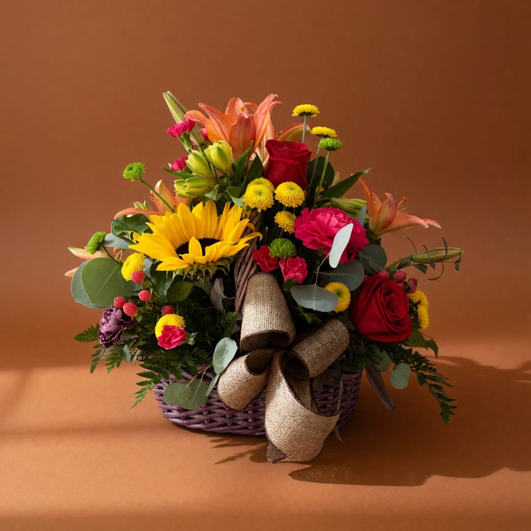 Mixed flower basket with roses, lilies, sunflower, and a burlap bow