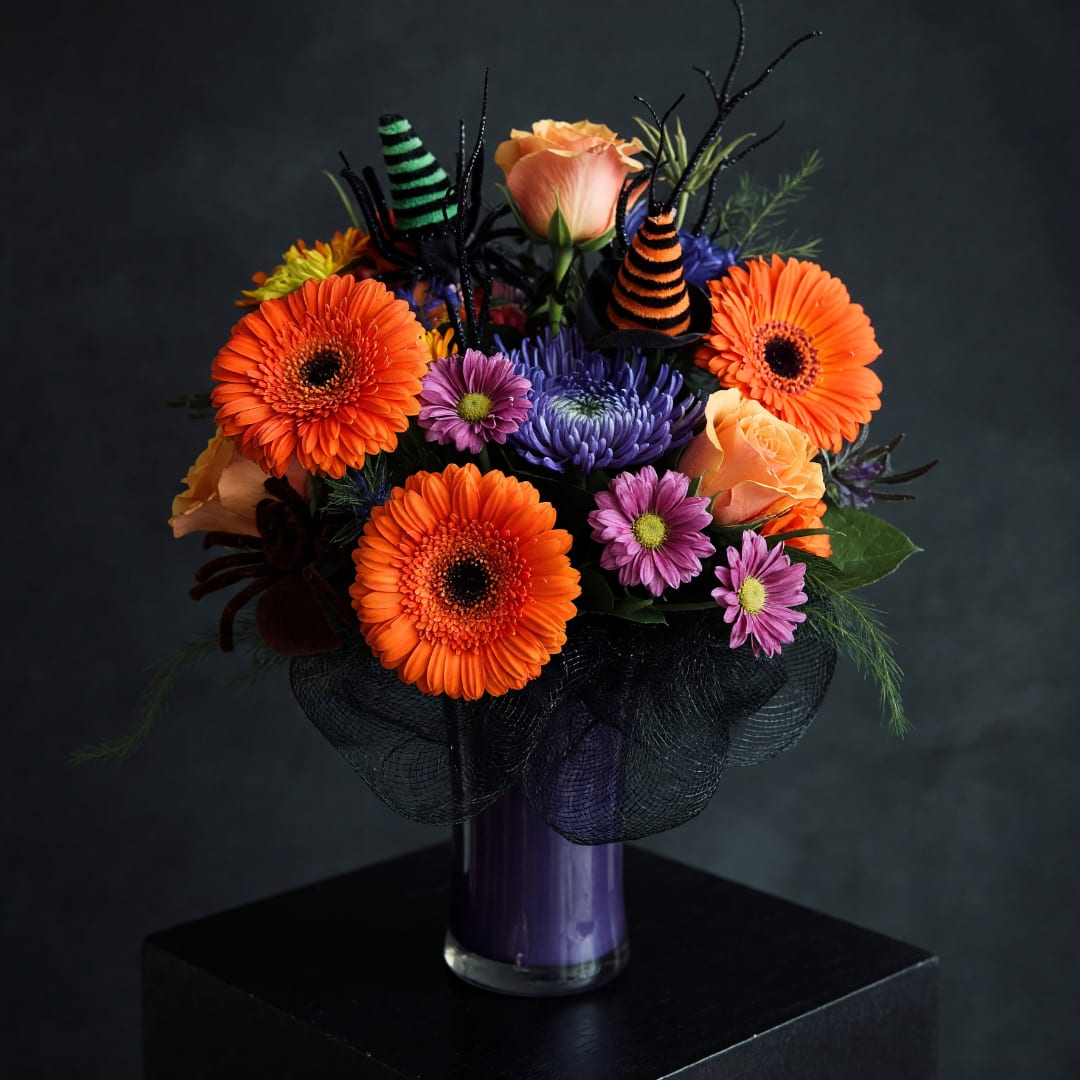 Orange gerbera daisies and roses in a purple vase with Halloween decorations