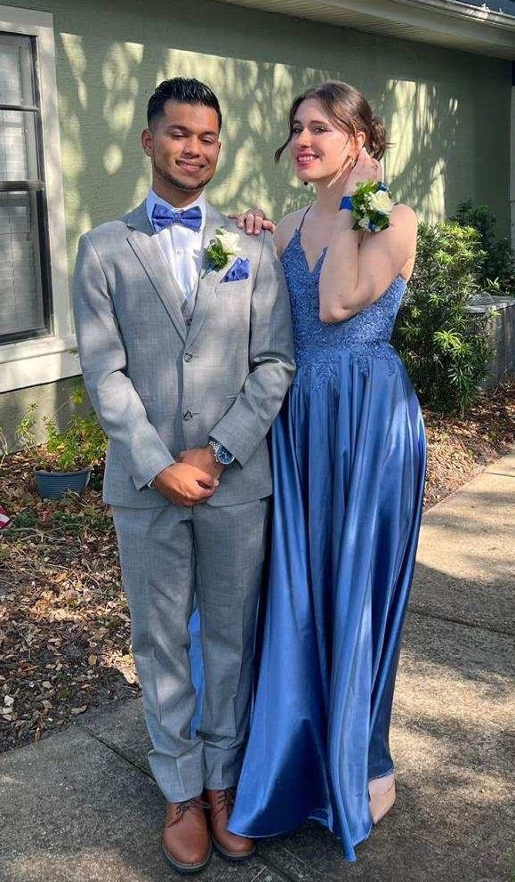 White rose wrist corsage and matching boutonniere with blue ribbon worn by a dressed-up couple.
