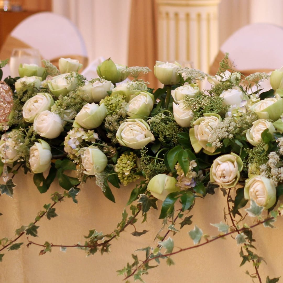 Low wedding centerpiece with cream roses and trailing ivy on a table