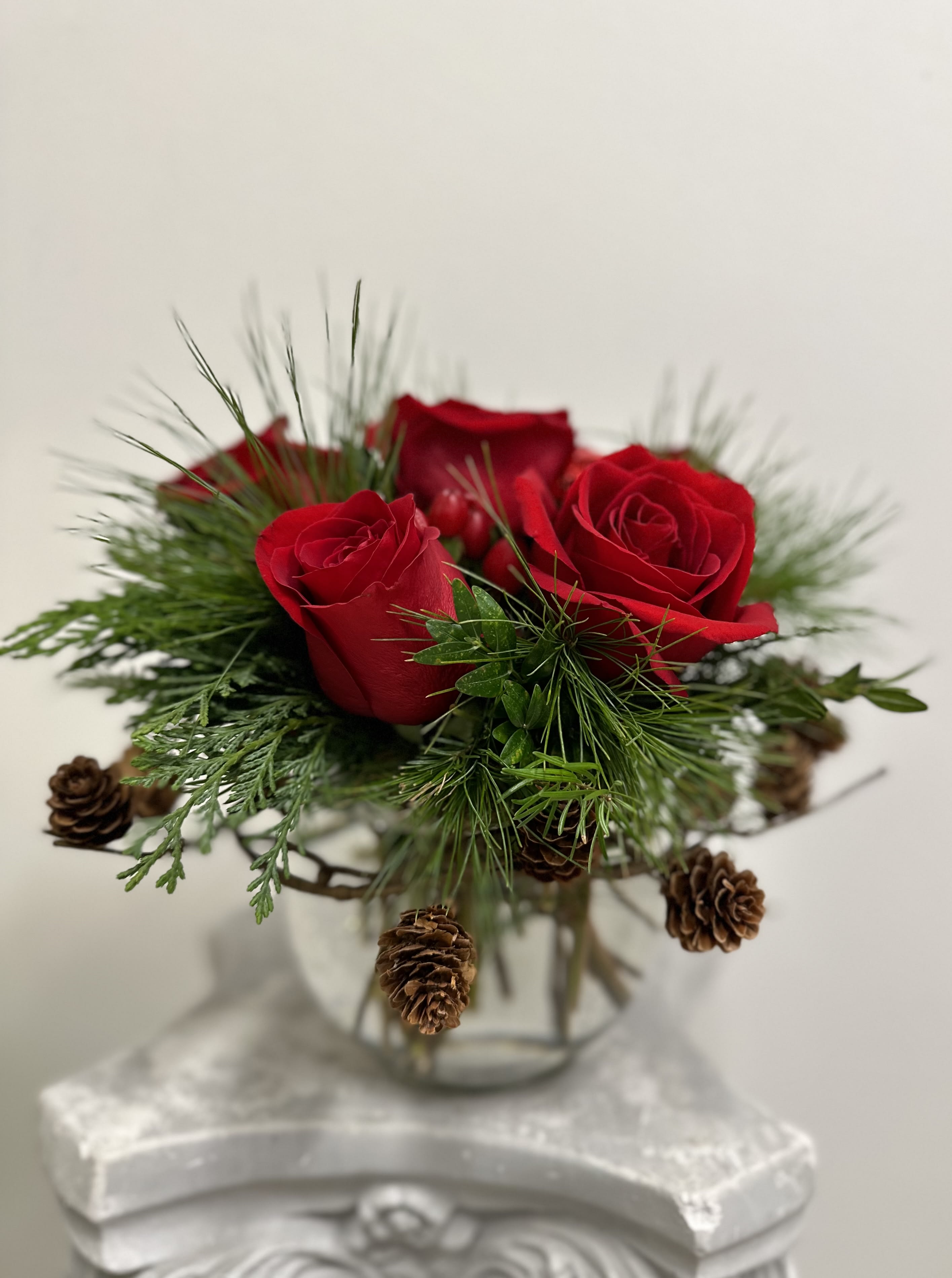 Peppermint Spice by Westford Florist Art by Veny - Embrace the enchanting spirit of the season with Peppermint Spice by Westford Florist Art by Veny. This exquisite arrangement features six stunning red roses, vibrant red berries, and fresh evergreens, thoughtfully crafted in a charming bubble bowl. The addition of a rustic pine cone wreath enhances its elegance while infusing your space with holiday cheer. Perfect for gifting or elevating your own décor, this floral masterpiece captures joy and warmth during this special time of year. Celebrate the magic of the season with Peppermint Spice—where beauty meets festive delight.