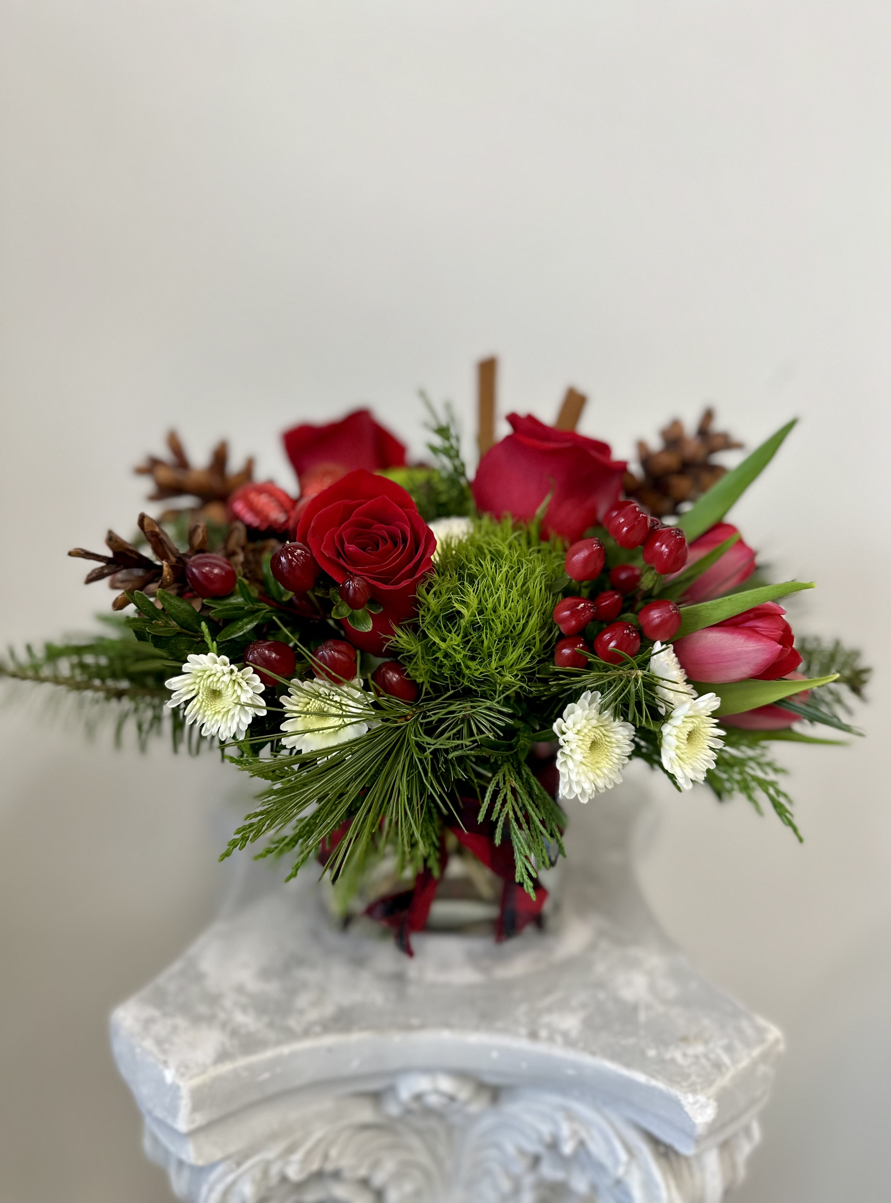 Seasonal Cheer by Westford Florist Art by Veny - Embrace the spirit of the season with Seasonal Cheer by Westford Florist Art by Veny. This exquisite floral arrangement features a harmonious blend of vibrant red, crisp white, and lush green blooms, creating a captivating centerpiece that brings warmth and joy to any holiday gathering. Each bouquet is artistically topped with real pinecones and festive ornaments, adding a touch of nature’s charm and seasonal flair. Perfect for your home or as a thoughtful gift, this elegant composition captures the essence of holiday cheer—making every moment special and memorable. Celebrate the season in style with this stunning floral masterpiece.
