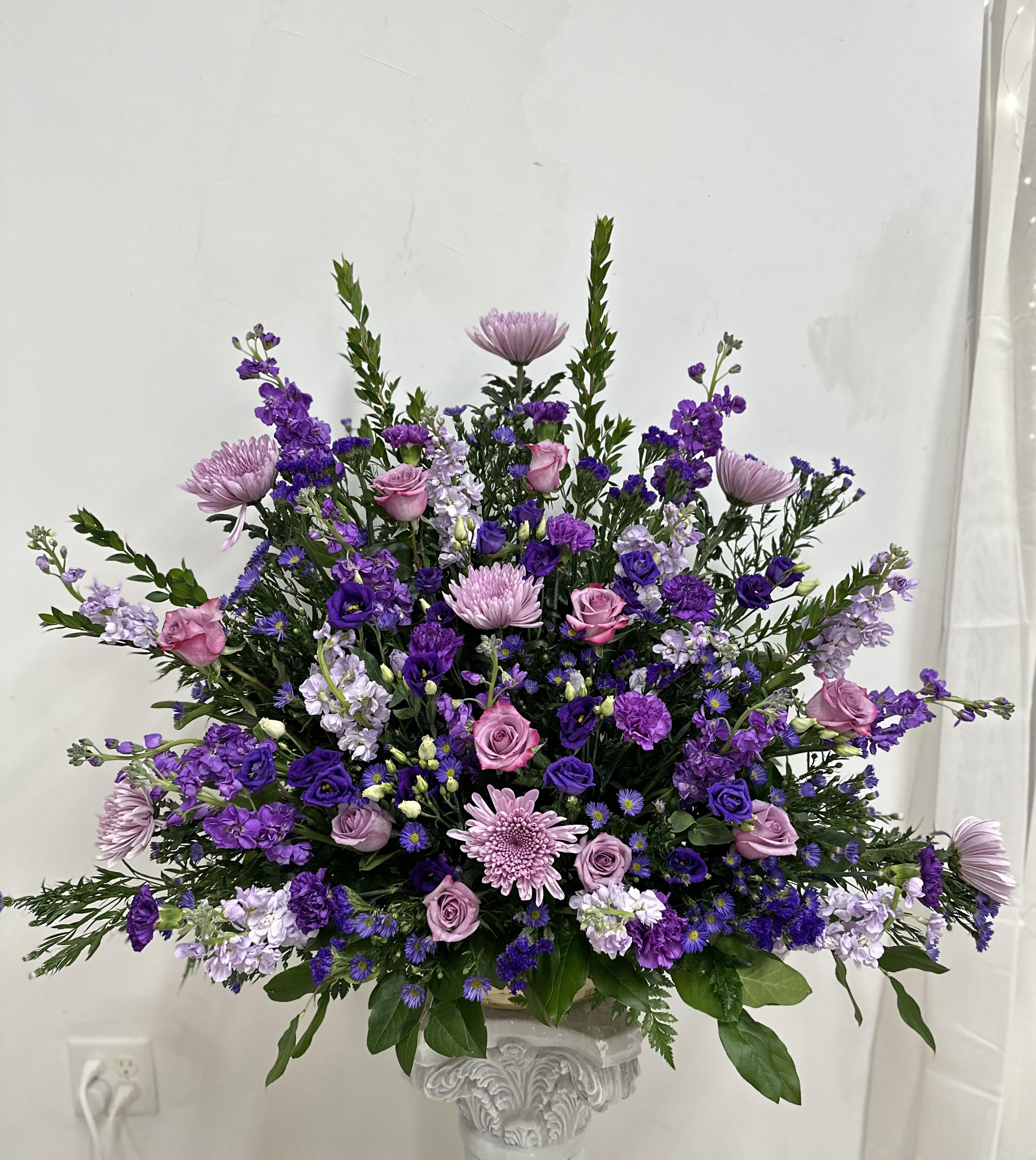 Large purple and pink floral arrangement in a decorative pedestal vase