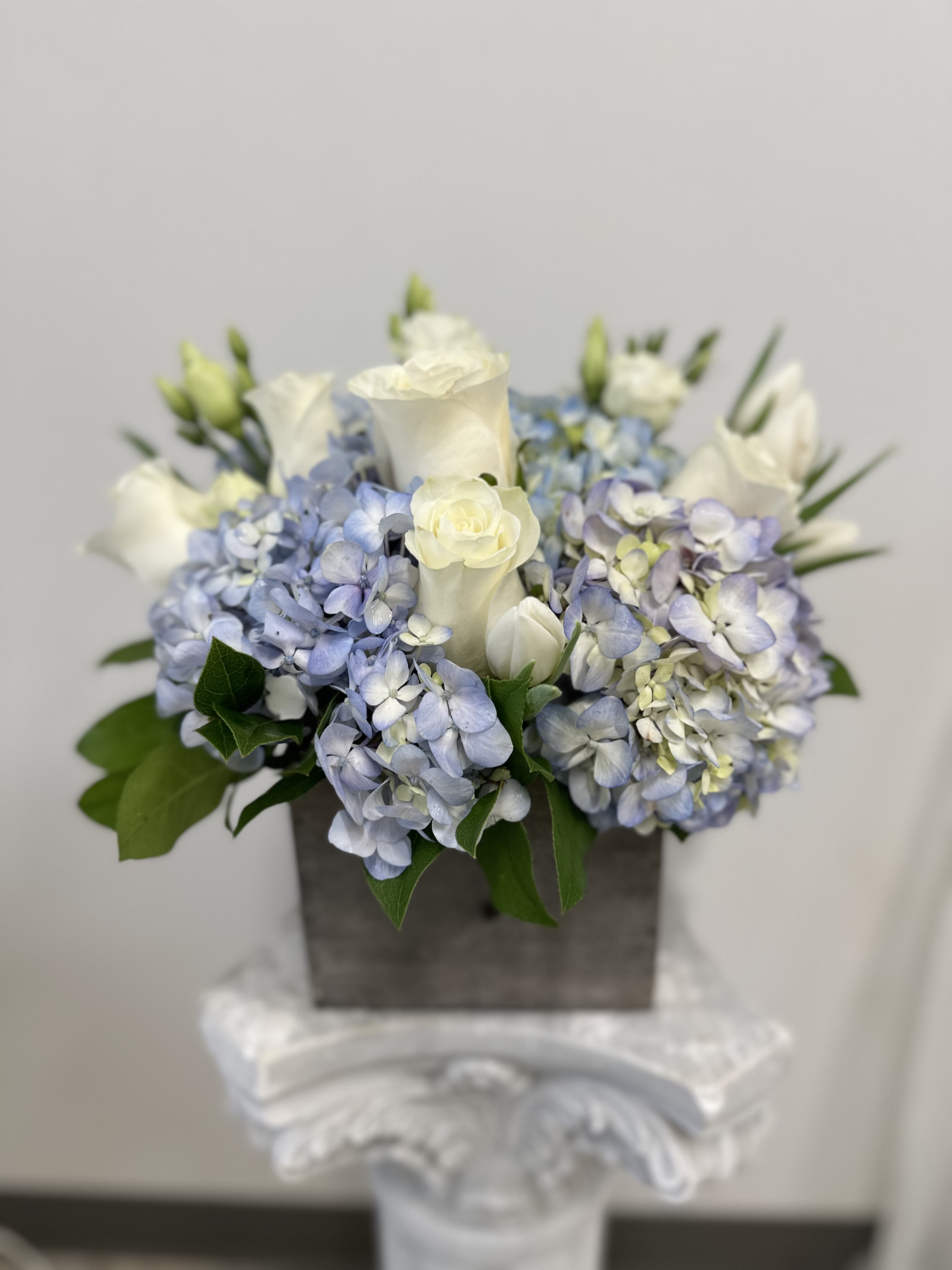 Compact arrangement of white roses and blue hydrangeas in a gray wooden box