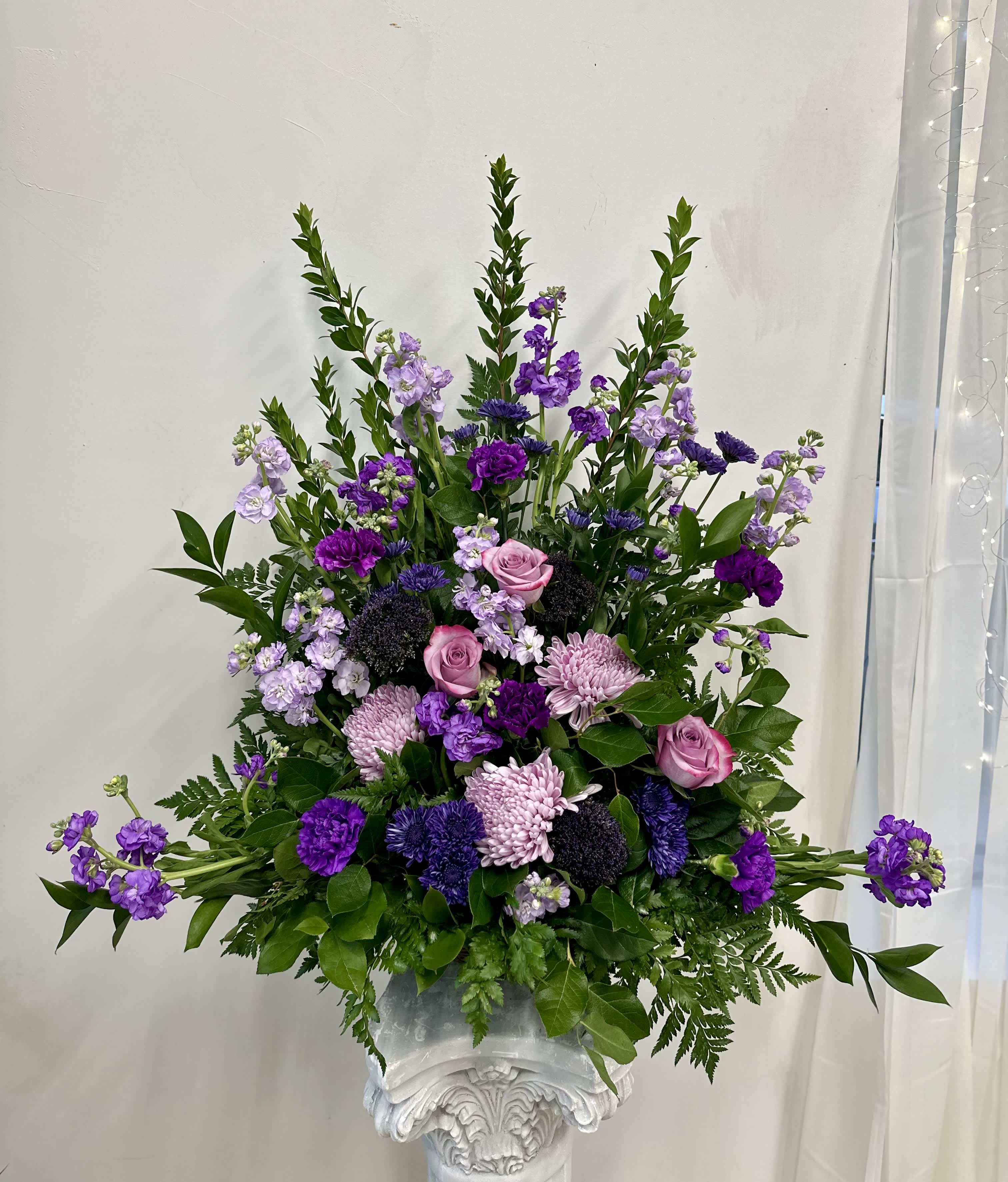 Tall purple and pink floral arrangement in a white pedestal vase