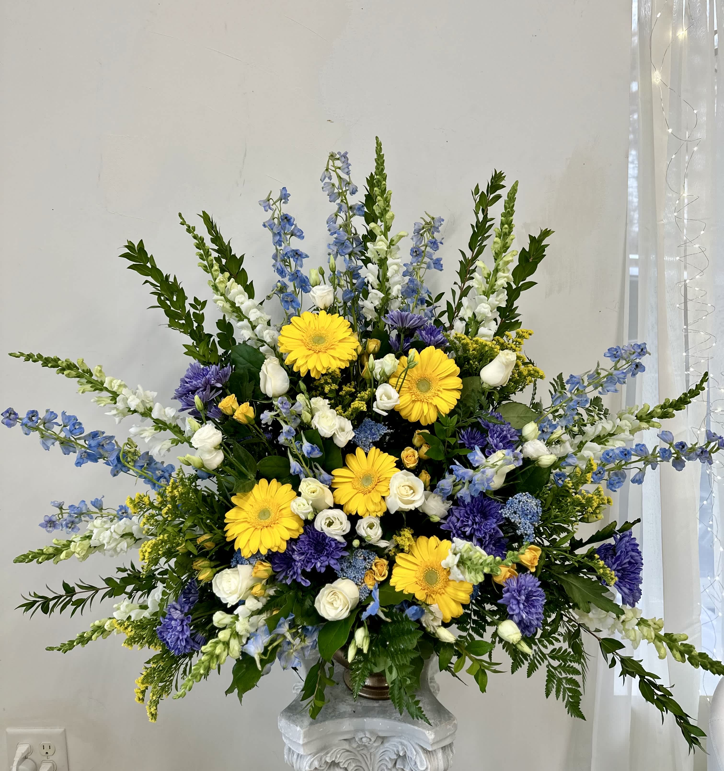 Large floral arrangement with yellow daisies, white roses, and blue-purple flowers in a vase