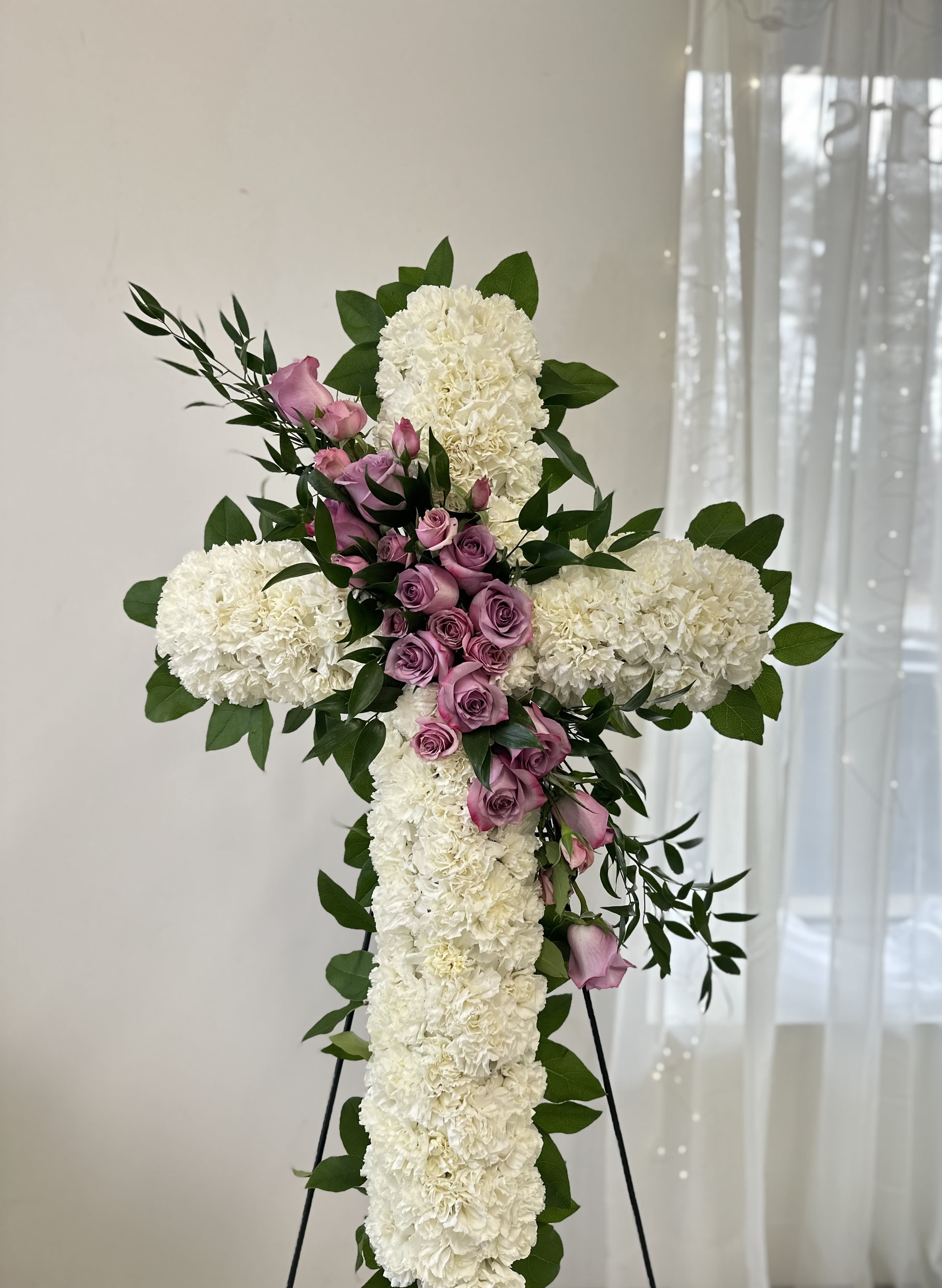 White floral cross with pink roses and greenery on a stand
