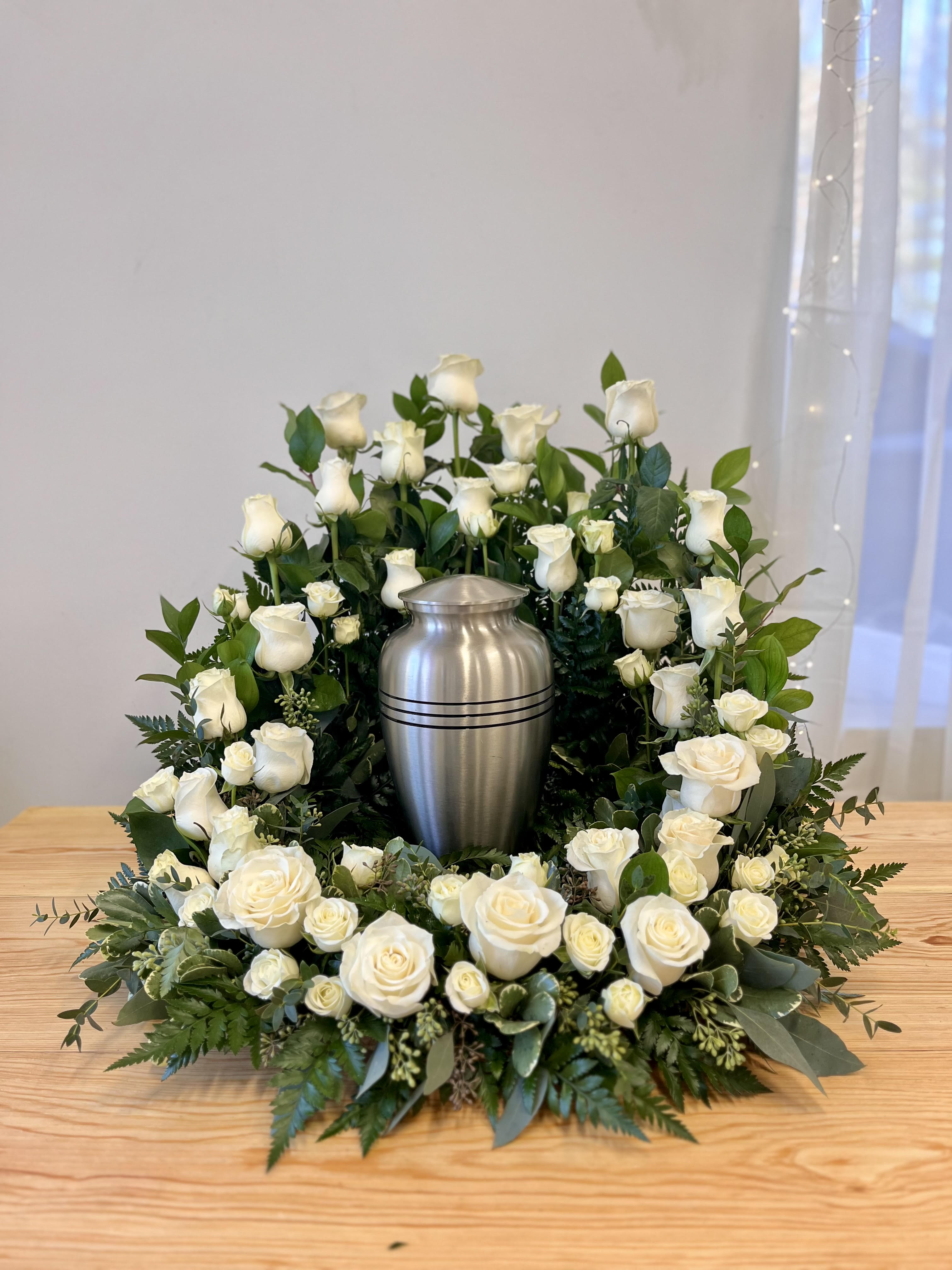 White rose wreath around a silver urn on a table