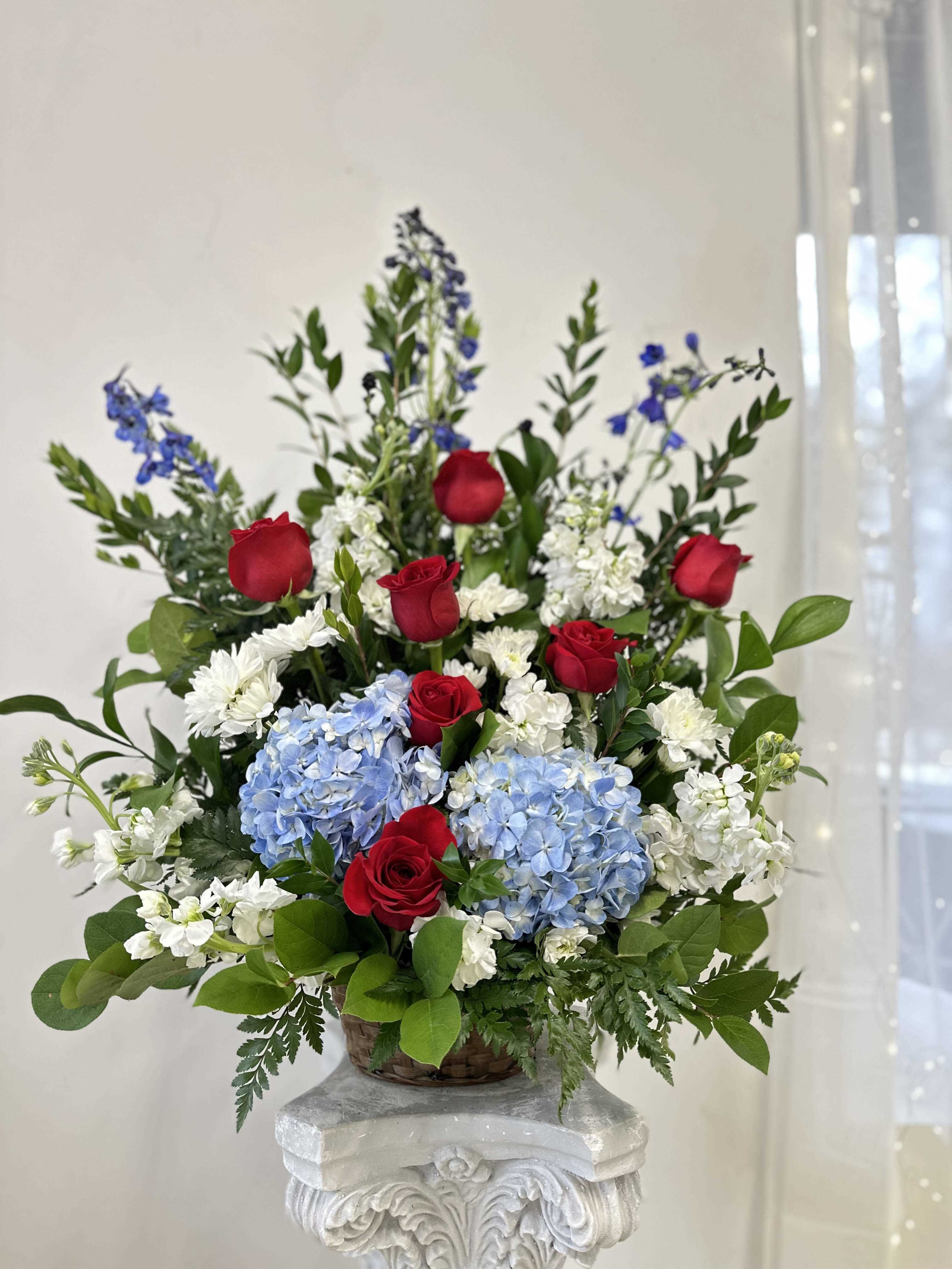 Red roses, blue hydrangeas, and white flowers in a basket arrangement