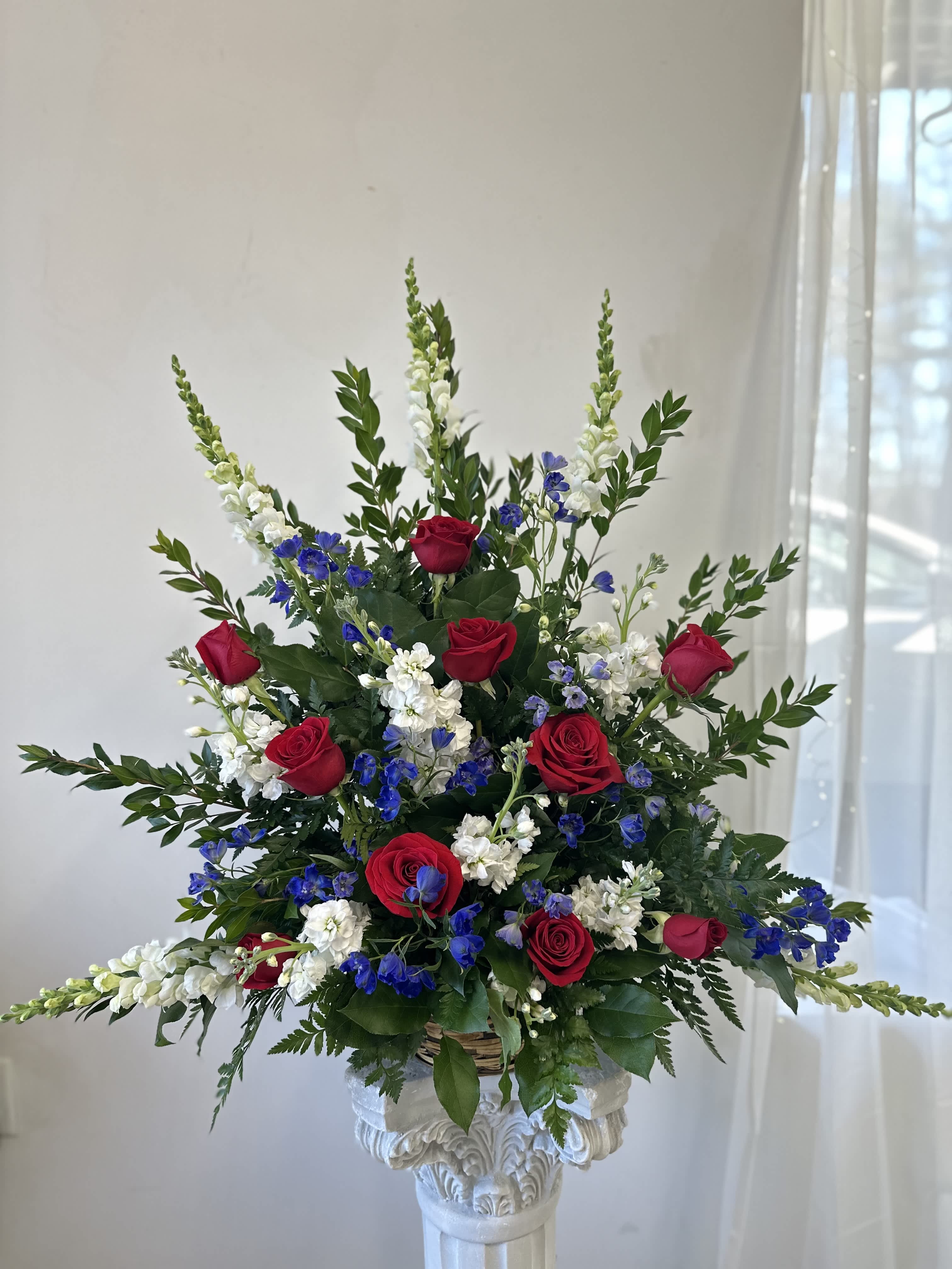 Tall arrangement of red roses, white snapdragons, and blue flowers in a basket