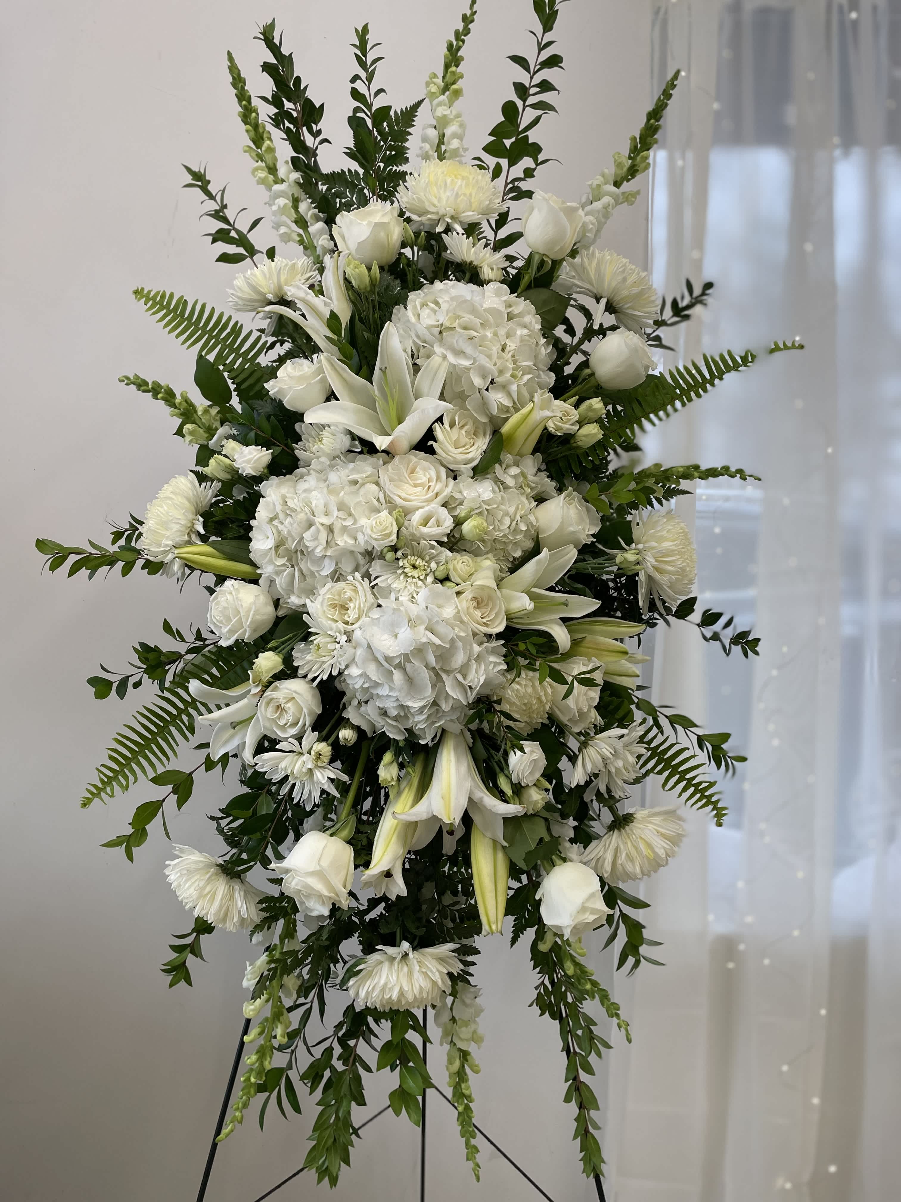 White funeral spray with lilies, roses, and hydrangeas on a stand