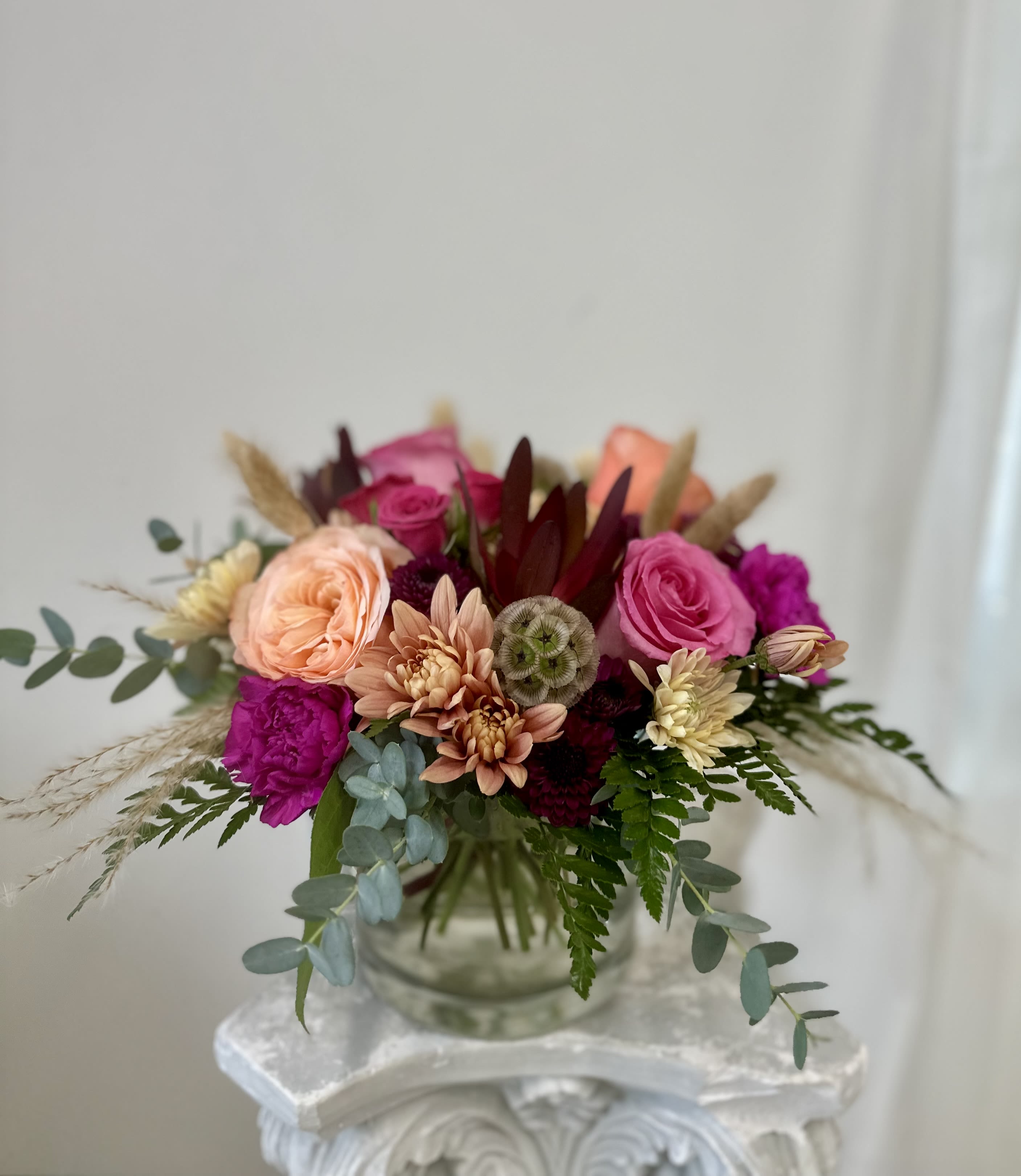 Peachy Burgundy Perfection by Westford Florist Art by Veny - For an elegant and sophisticated touch to your next special occasion, look no further than Westford Florist Art by Veny Peachy Burgundy Perfection floral arrangement. This stunning creation boasts a blend of delicate Roses, gorgeous Poms, lush safari sunset, and curated dry flowers for an unforgettable experience. The primary focal point is the soft peach Roses with subtle burgundy accents, symbolizing love and passion. Complementing them are the rich burgundy Poms, representing joy and happiness. Bring in a sense of adventure and excitement with vibrant safari sunsets, symbolizing strength and perseverance. To add texture and beauty, our arrangement features dry flowers like the full-bodied spray rose in pale pink, deep burgundy carnations for drama and admiration, mums in striking purple hues, and whimsical Scabiosa pods for intricate details. Perfect for any milestone celebration or expression of gratitude towards someone special. Every blossom in this carefully crafted arrangement has been carefully chosen to come together in perfect harmony.