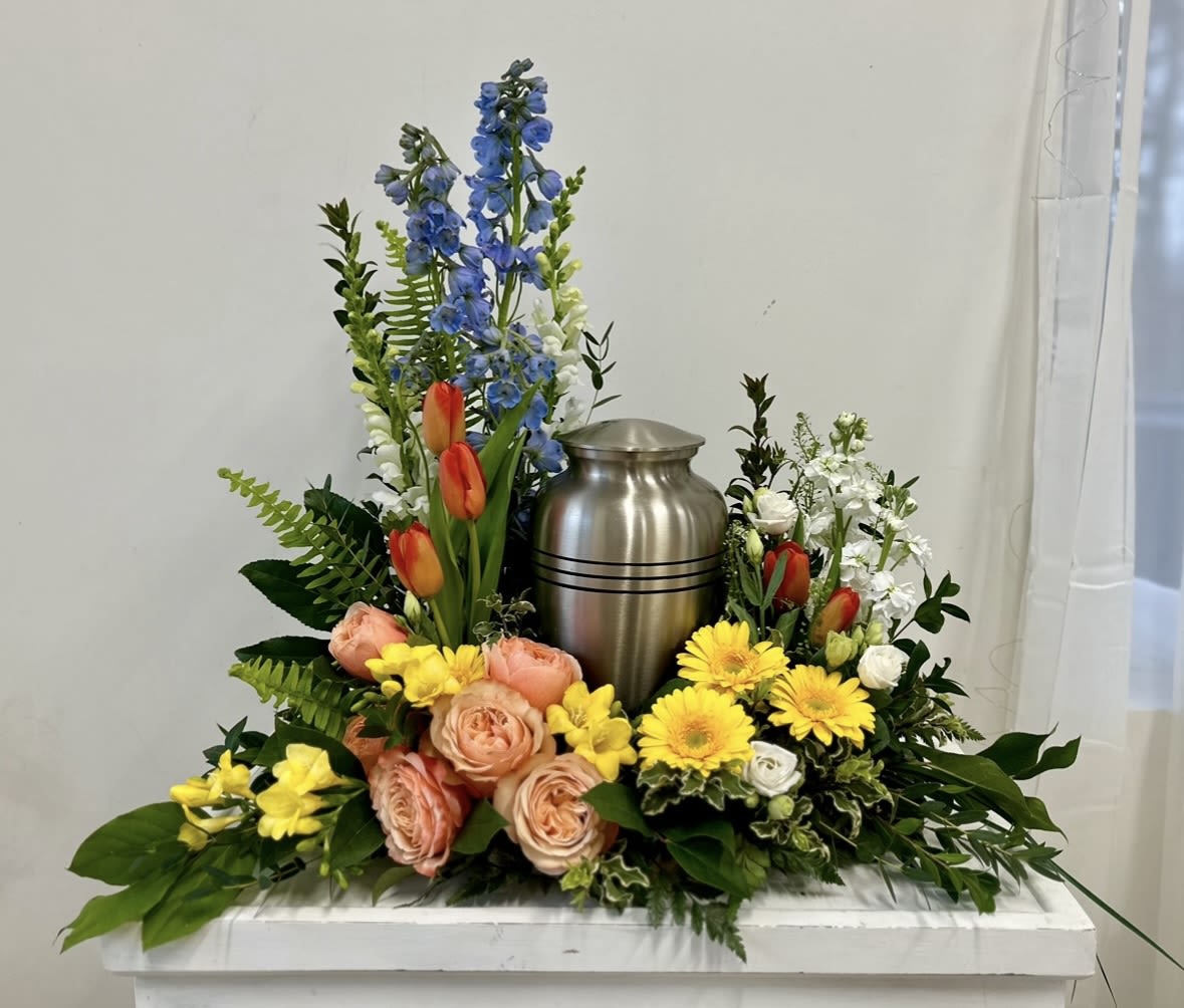 Floral urn arrangement with blue delphinium, tulips, roses, and yellow daisies