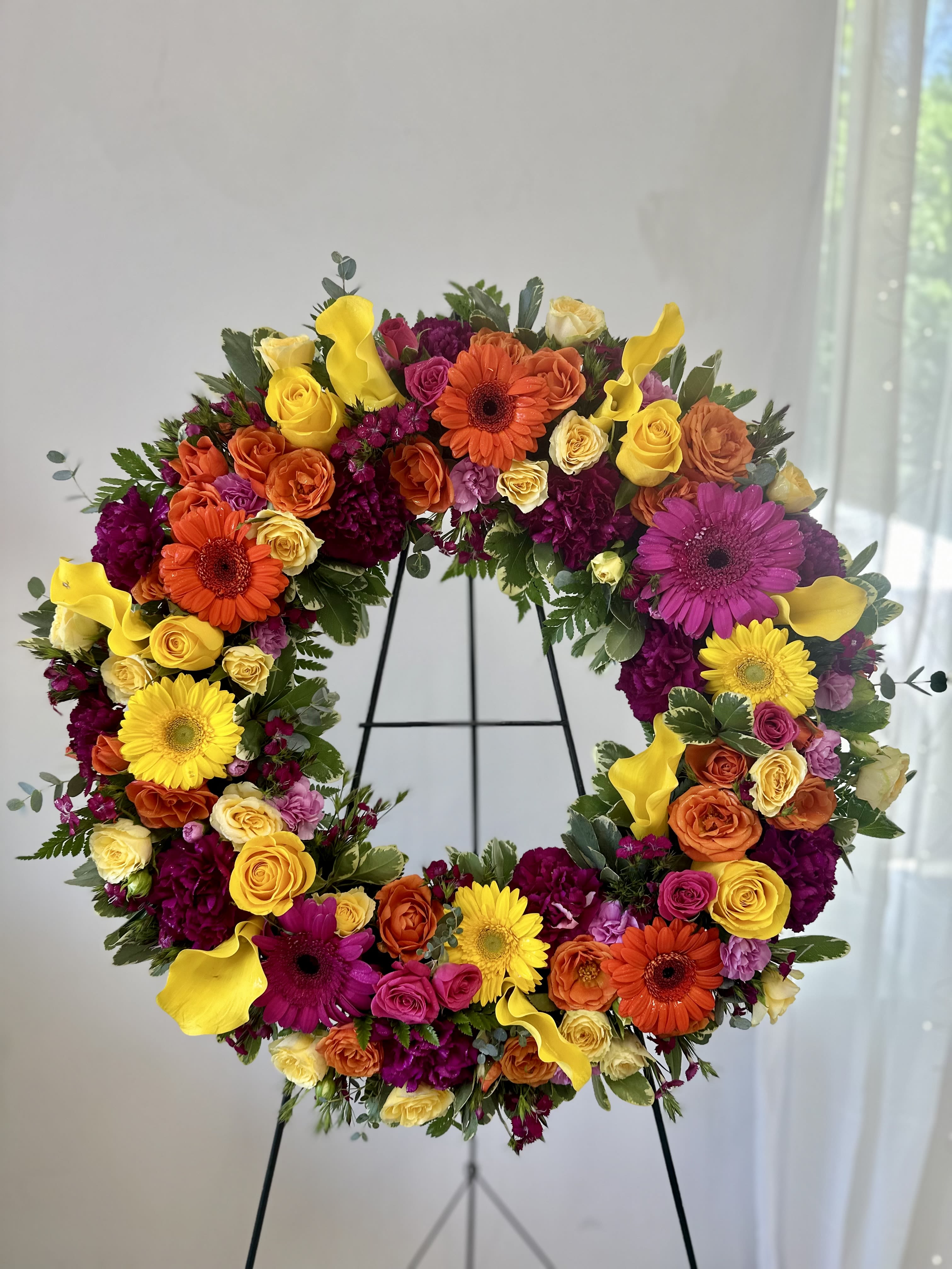 Large circular floral wreath on a stand with yellow, orange, pink, and purple blooms