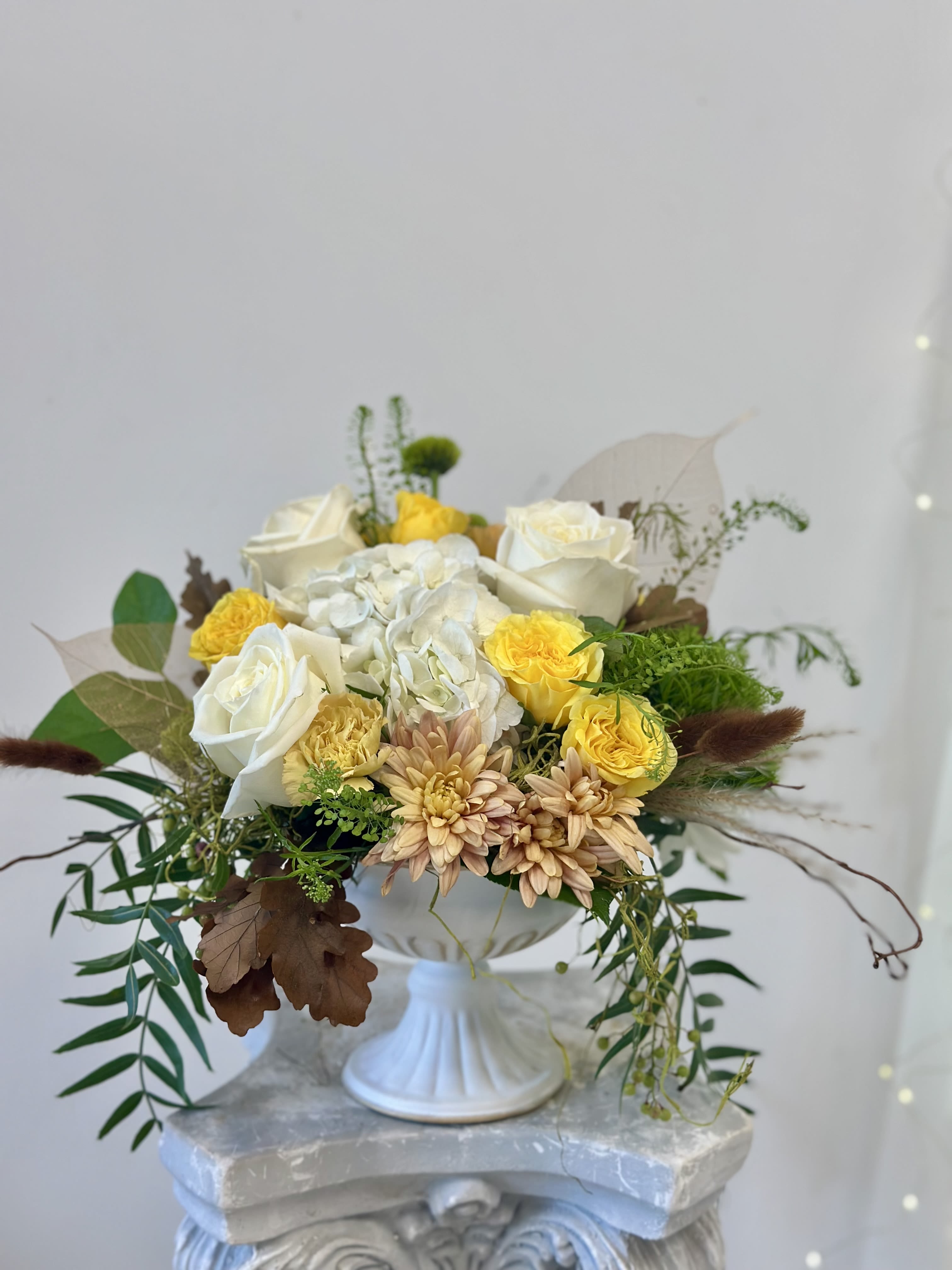 Whimsical Wonderland by Westford Florist Art by Veny - Step into a captivating realm of beauty with Whimsical Wonderland by Westford Florist Art by Veny, a stunning floral arrangement that transforms any space into an enchanting retreat. This exquisite composition features elegant white roses and hydrangeas delicately paired with cheerful yellow spray roses and delightful green accents. The addition of charming peach poms, pepper berries, curly willow, dried oak leaves, and soft brown bunny tails creates a harmonious blend that speaks to nature’s artistry. Presented in an elegantly washed white pedestal metal vase, this arrangement is perfect for elevating your décor—be it for special occasions or simply to brighten up your everyday surroundings. Whimsical Wonderland invites you to indulge in the serenity of sophisticated floral design while celebrating life’s delicate moments. Enhance your environment today with this truly mesmerizing centerpiece.