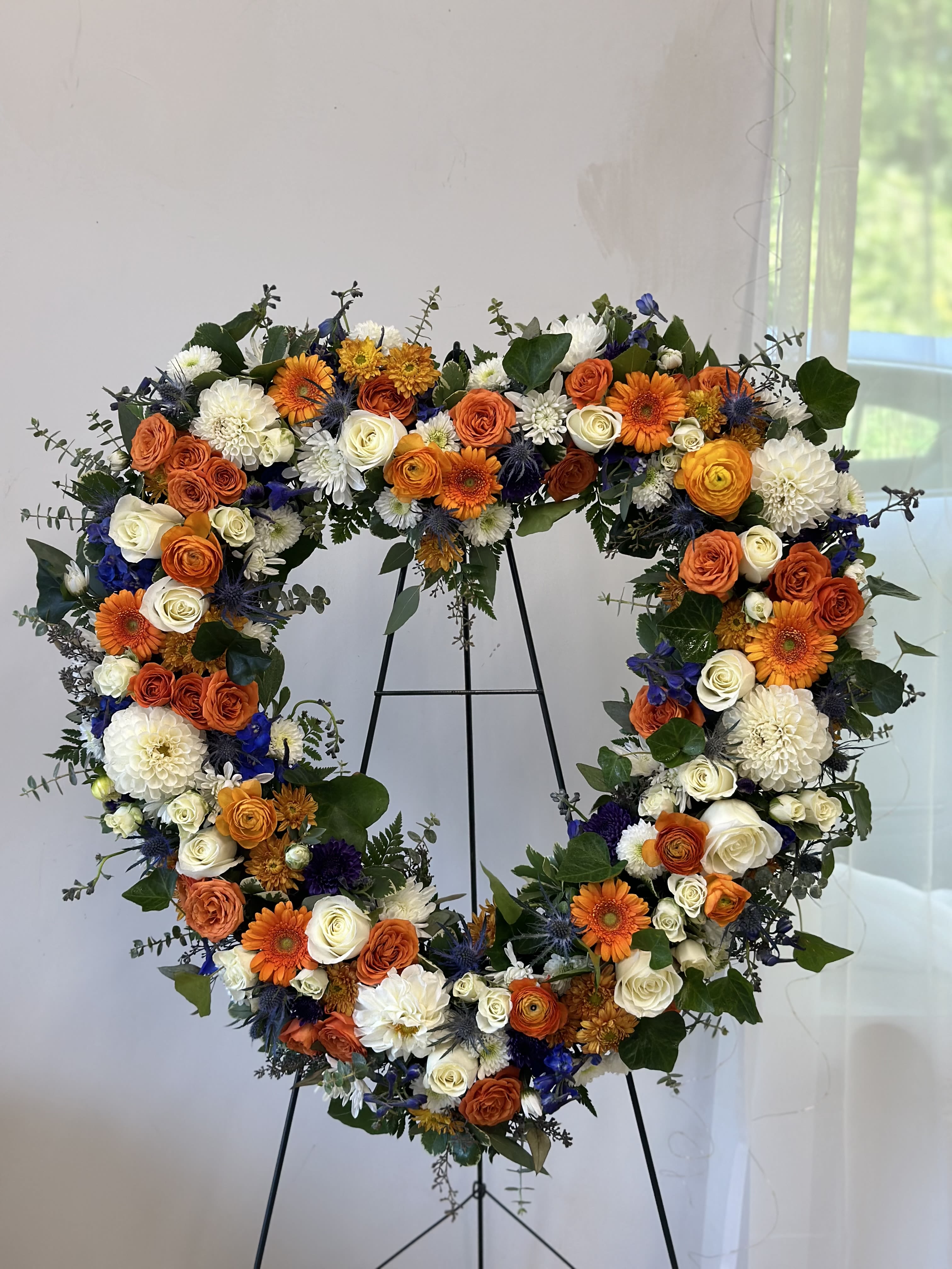Heart-shaped floral wreath with orange, white, and blue flowers on a stand