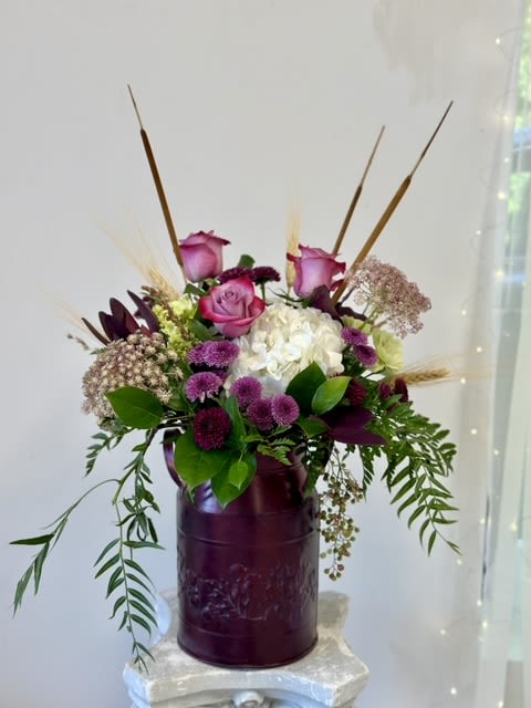 Whimsical Fall Garden by Westford Florist Art by Veny - Elevate your seasonal décor with the Whimsical Fall Garden by Westford Florist Art by Veny. This exquisite arrangement artfully combines lavender roses and lush hydrangeas, underscored by delicate Queen Anne’s lace for an enchanting touch. Cheerful lavender mini button pom pop against a backdrop of warm safari sunset foliage, bringing warmth and depth to any space. The addition of whimsical fall weeds and cat tails evokes nature's charm, perfectly encapsulating autumn's beauty. Presented in a striking tall red tin vase, this stunning floral ensemble not only enhances your home but also makes a thoughtful gift for loved ones. Experience the essence of fall with this captivating display that transforms any setting into a celebration of the season.