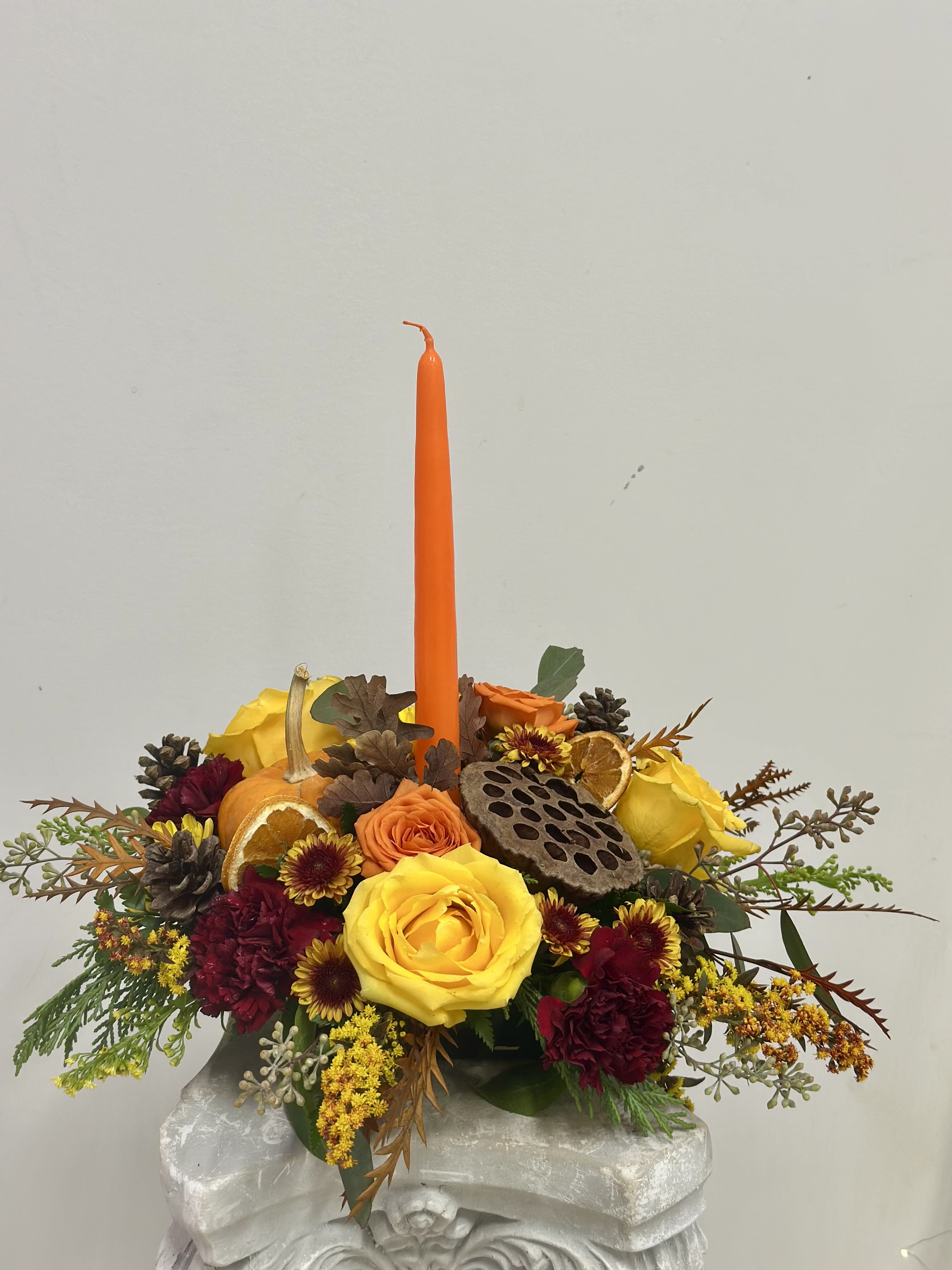 Harvest Glow Centerpiece by Westford Florist Art by Veny - Elevate your holiday festivities with the Harvest Glow Centerpiece from Westford Florist Art by Veny. This stunning arrangement includes a mix of vibrant orange and yellow roses, accompanied by charming mini pumpkins, hypericum berries, and lush fall foliage. The centerpiece features tall candles that provide a warm ambiance for any gathering. For an added touch of opulence, our premium option includes delicate orchids to elevate the overall aesthetic. Make your table the focal point of the holiday season with this tastefully designed centerpiece that embodies both gratitude and elegance. Embrace the spirit of gratitude and togetherness with a stunning centerpiece that reflects the warmth of the season. Transform your space with perfect blend of elegance and seasonal charm that reflects the spirit of harvest season.