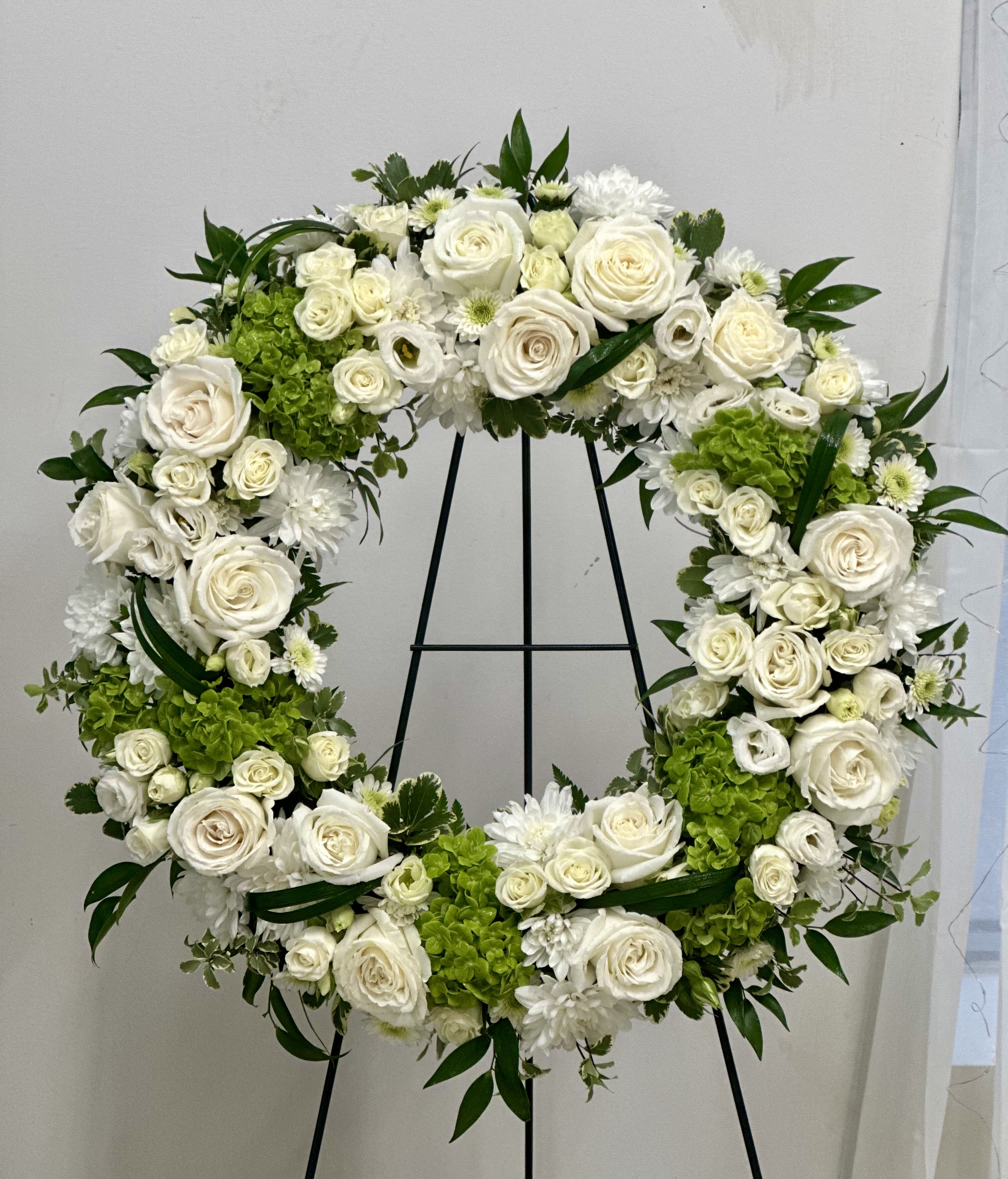 White floral wreath on a black stand with green accents
