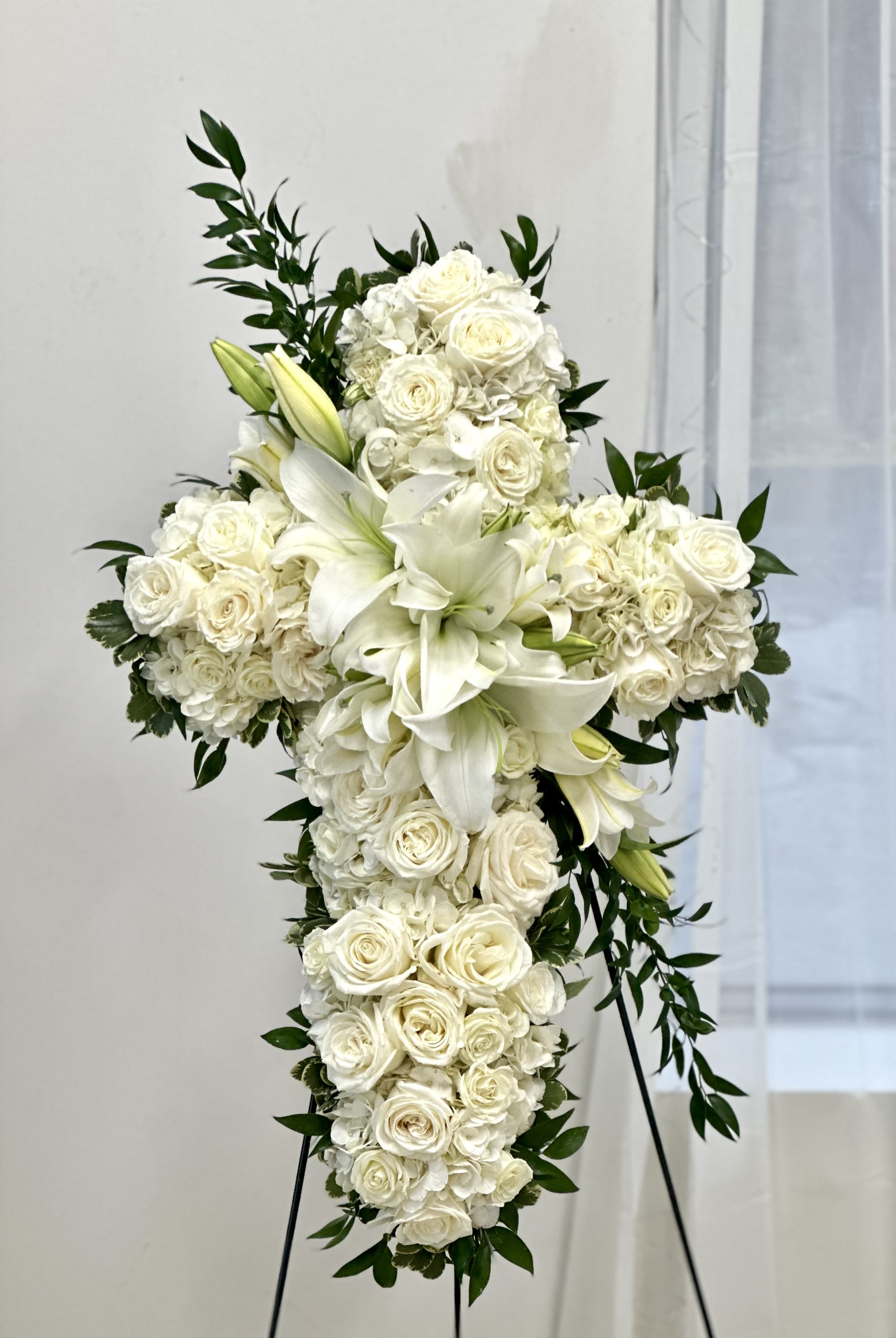White floral cross on a stand with lilies and roses