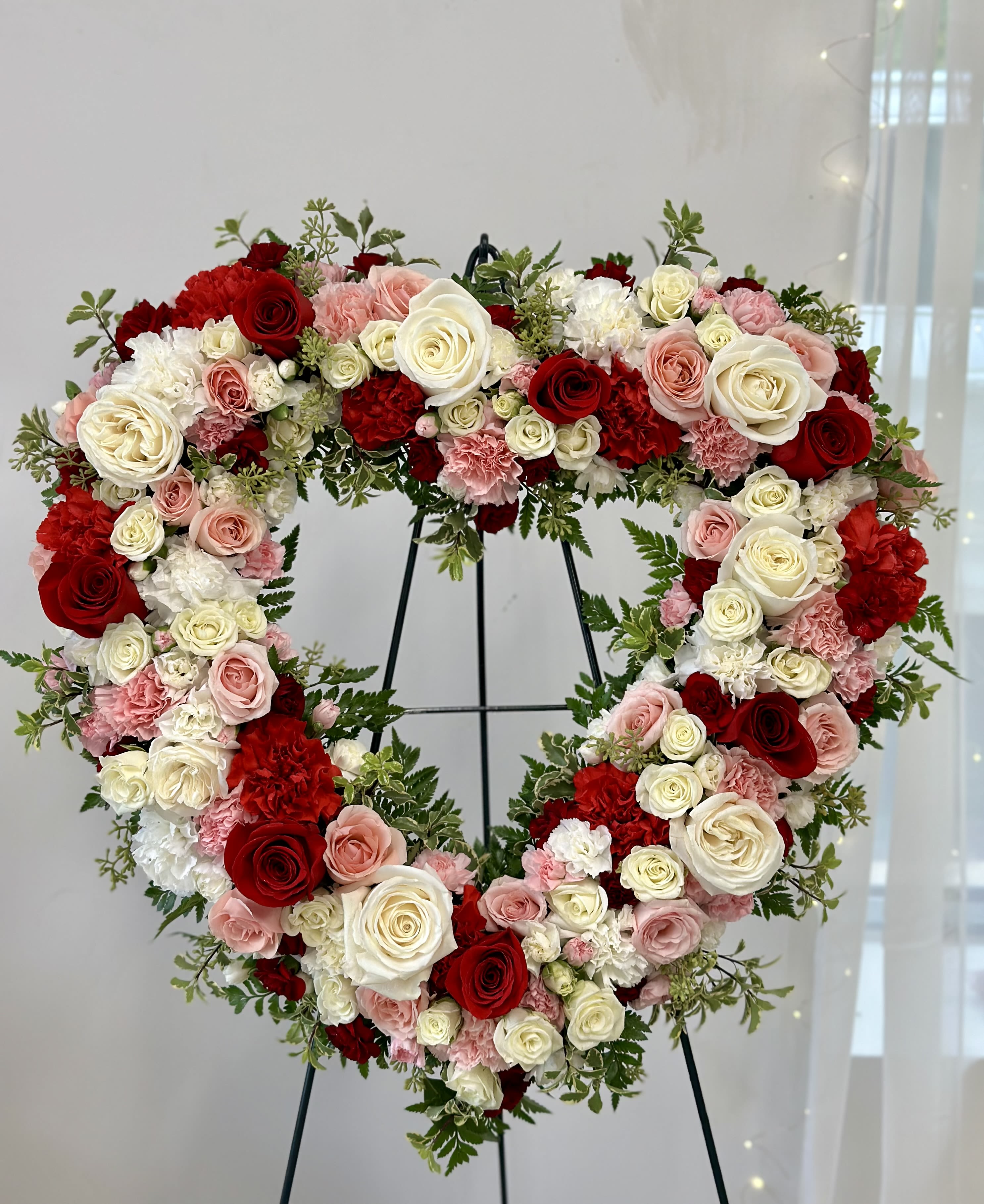 Heart-shaped floral wreath of red, pink, and white roses on a stand