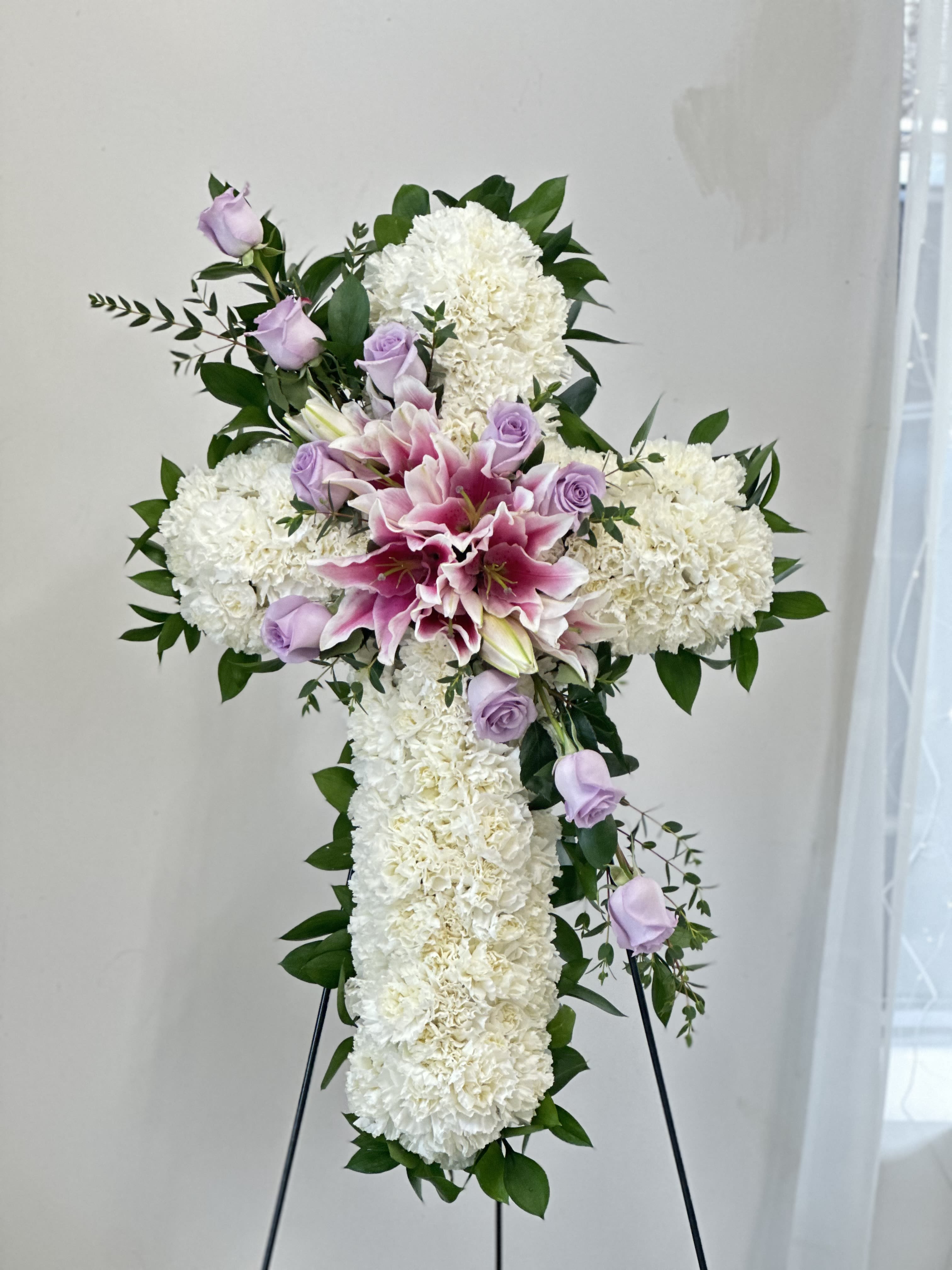 White floral cross with pink lilies and lavender roses on an easel