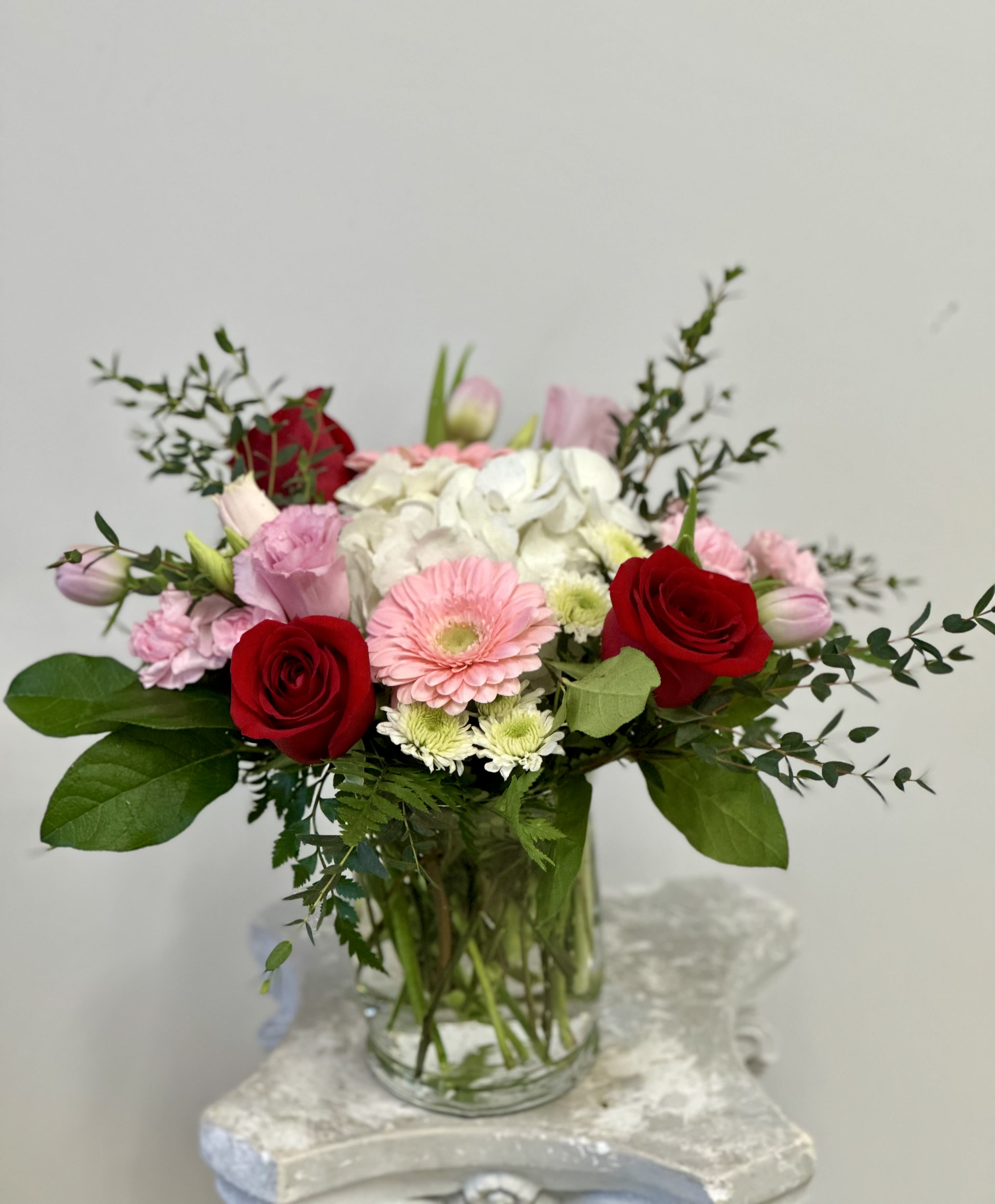 Romantic Elegance by Westford Florist Art by Veny - Indulge in a symphony of romance with the Romantic Elegance arrangement by Westford Florist Art by Veny. This exquisite bouquet showcases an enchanting blend of velvety red roses, ethereal hydrangeas, and vibrant gerberas, gracefully intertwined with tender tulips, elegant lisianthus, playful dot poms, and charming mini carnations. Each bloom is lovingly cradled amidst sumptuous greenery, all elegantly displayed in a sophisticated glass vase that adds a touch of opulence to any setting. Transform your Valentine's Day into an unforgettable celebration of love and beauty. Perfect for expressing deep emotions or simply indulging in life's luxuries, this stunning floral masterpiece promises to captivate hearts and ignite passions like never before. Elevate your gifting experience—because true elegance is timeless.