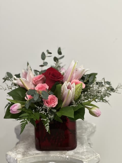 Velvet Romance by Westford Florist Art by Veny - Indulge in the exquisite allure of Velvet Romance by Westford Florist Art by Veny, a lavish bouquet that captures the essence of love. This breathtaking arrangement showcases velvety red roses and delicate spray roses, harmoniously intertwined with radiant lilies and vibrant tulips. Soft sea lavender peeks through lush greenery, creating a tapestry of color and fragrance that enchants the senses. Presented in an elegant glass red cube vase, this masterpiece transforms any space into a sanctuary of romance. Perfect for celebrating your deepest affections this Valentine’s Day or to simply spoil someone special, let Red Velvet Romance be the epitome of your heartfelt wishes—a gift as enchanting as love itself.