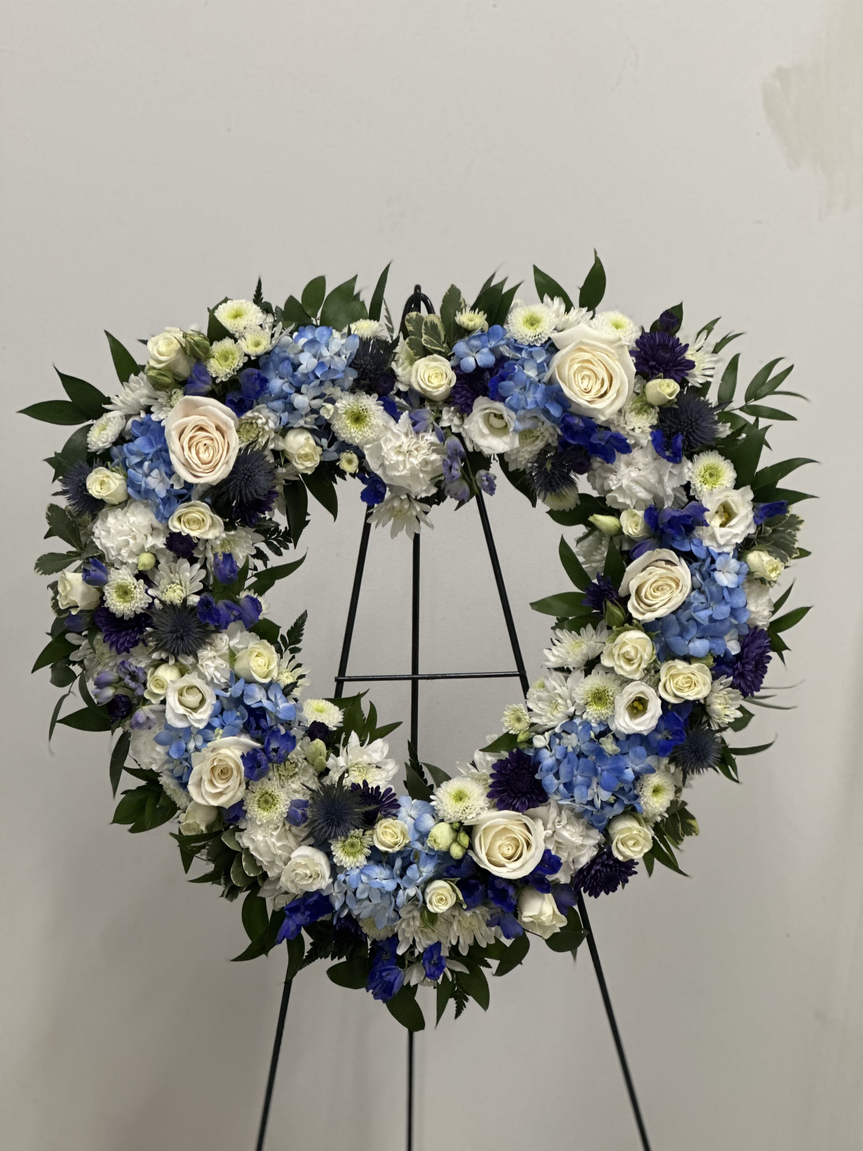 Heart-shaped floral wreath with blue, white, and cream flowers on a stand