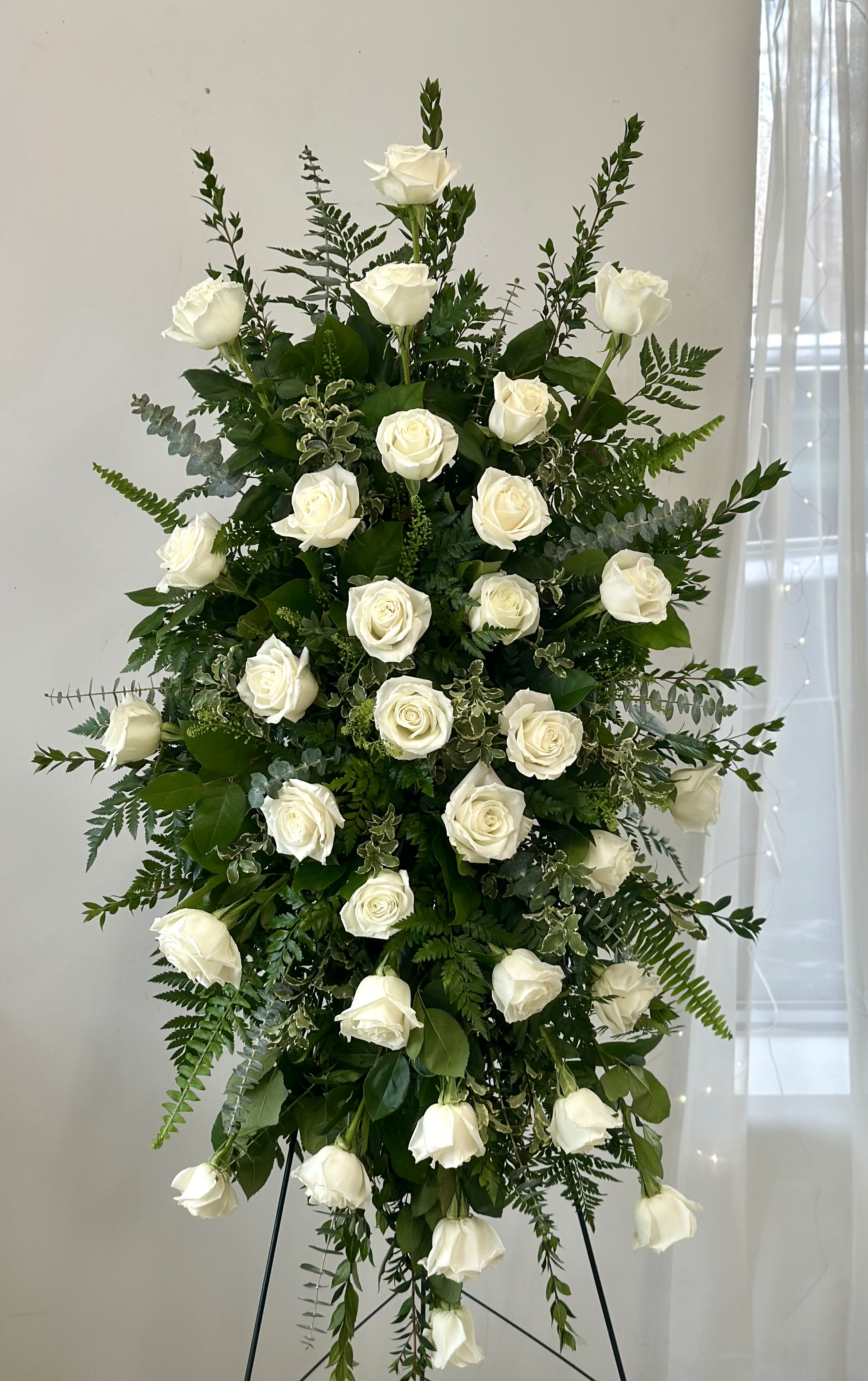 Tall standing arrangement of white roses and greenery on a black easel
