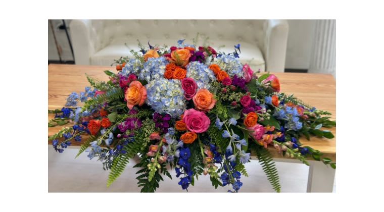 Large colorful floral centerpiece with roses and blue hydrangeas on a table