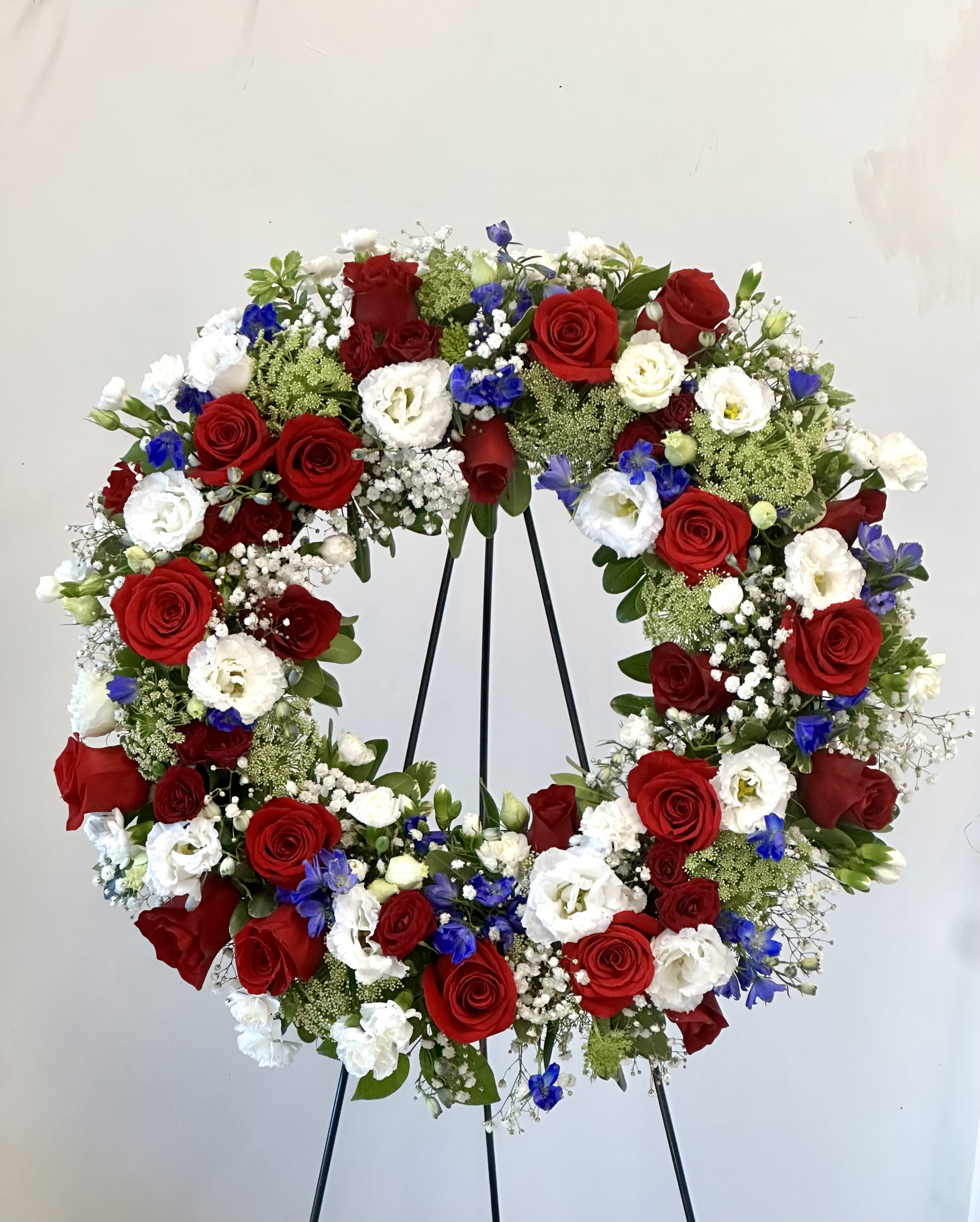 Heart-shaped wreath of red, white, and blue flowers on a black stand