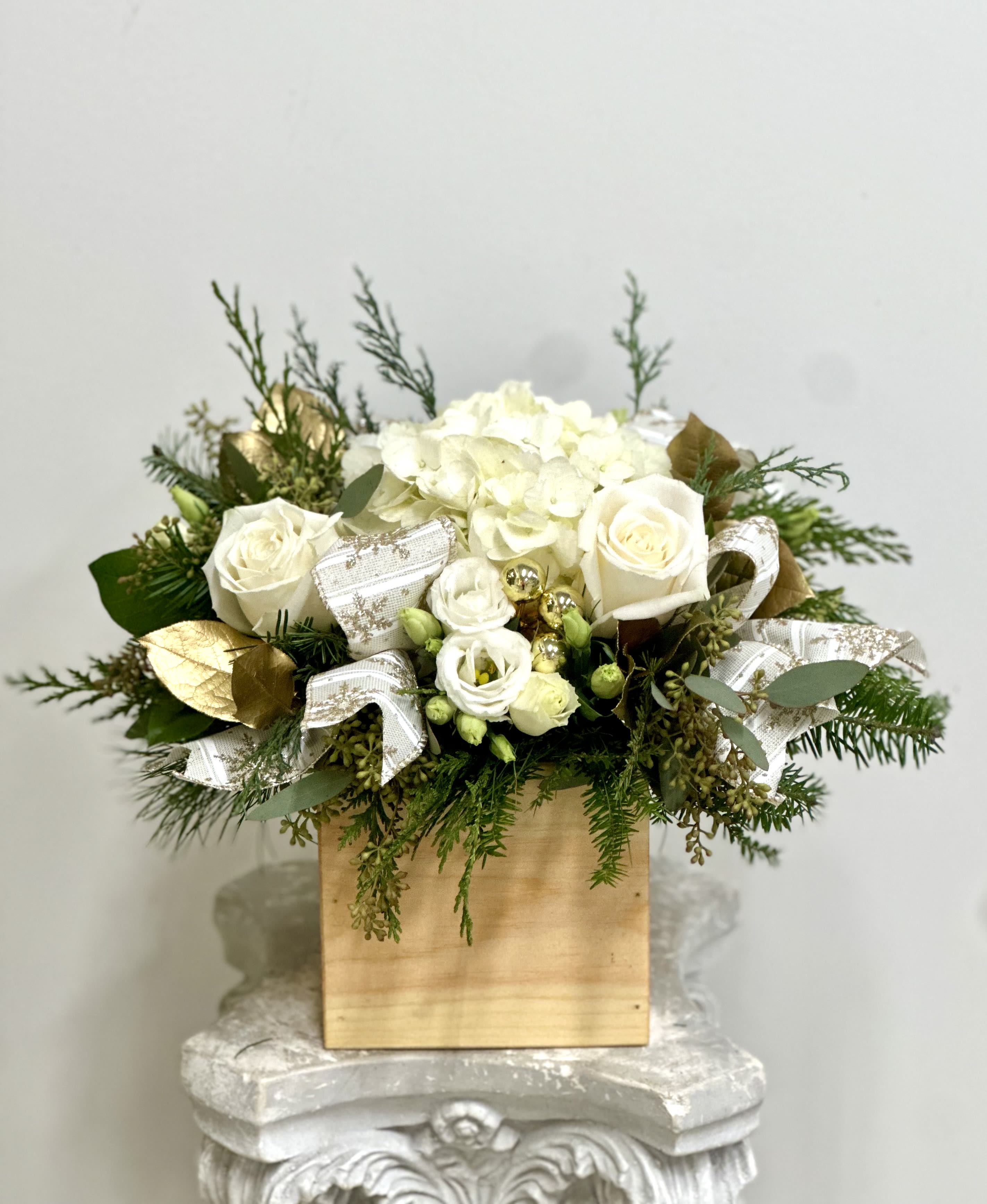 White Christmas by Westford Florist Art by Veny - Elevate your dining experience with White Christmas by Westford Florist Art by Veny. This stunning centerpiece, meticulously crafted from an exquisite blend of white hydrangea, lisianthus, snapdragon, lilies, and roses, exudes sophistication and charm. Nestled in a natural handmade wooden box made of white cedar, this arrangement not only captivates the eye but also complements any décor. Perfect for dinner gatherings or as a thoughtful holiday gift, White Christmas transforms any setting into a refined oasis. Impress your guests with its timeless beauty—a true testament to elegance that beckons attention and admiration. Make every occasion memorable with this luxurious floral display.