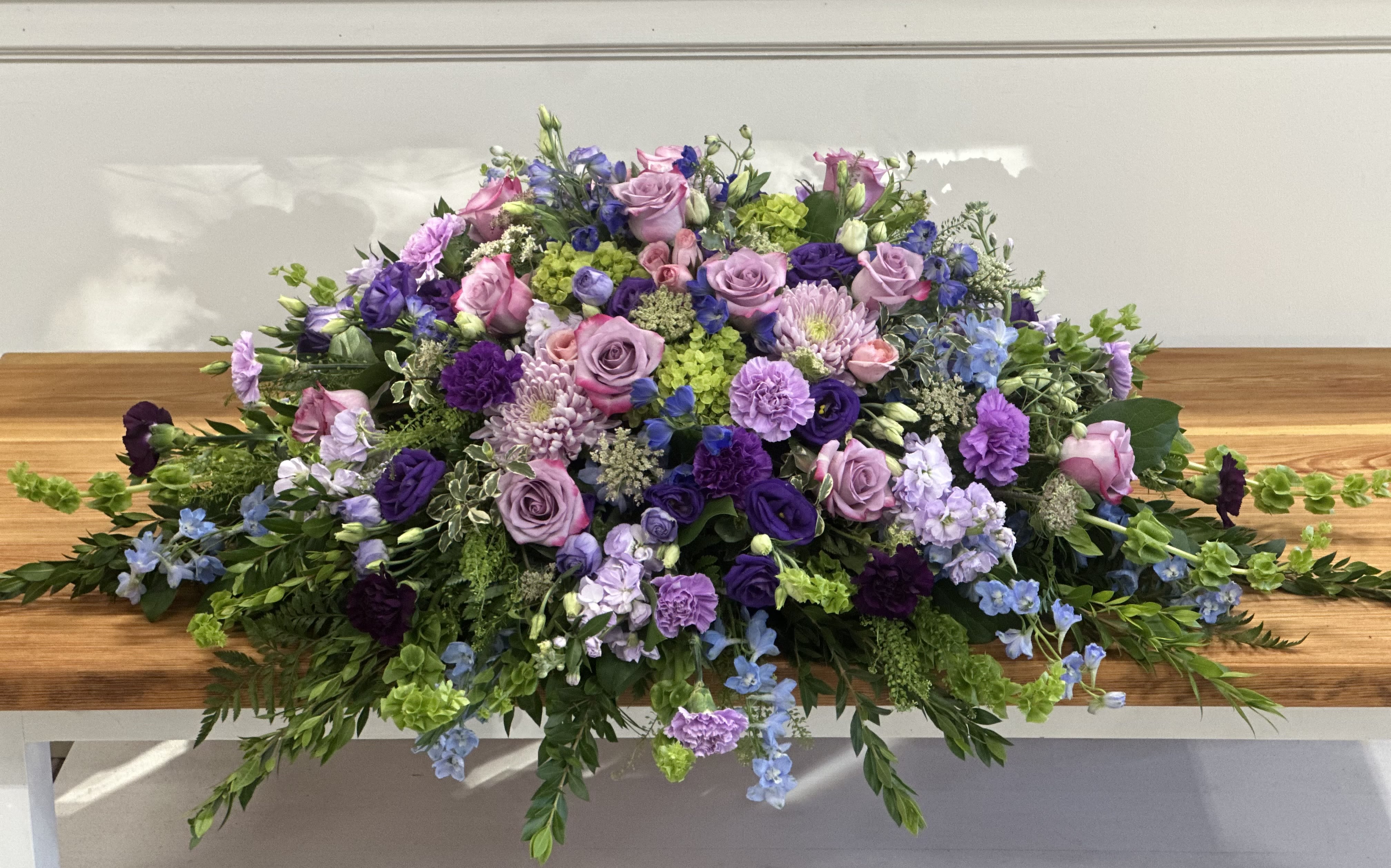 Large purple and pink floral casket spray with trailing greenery