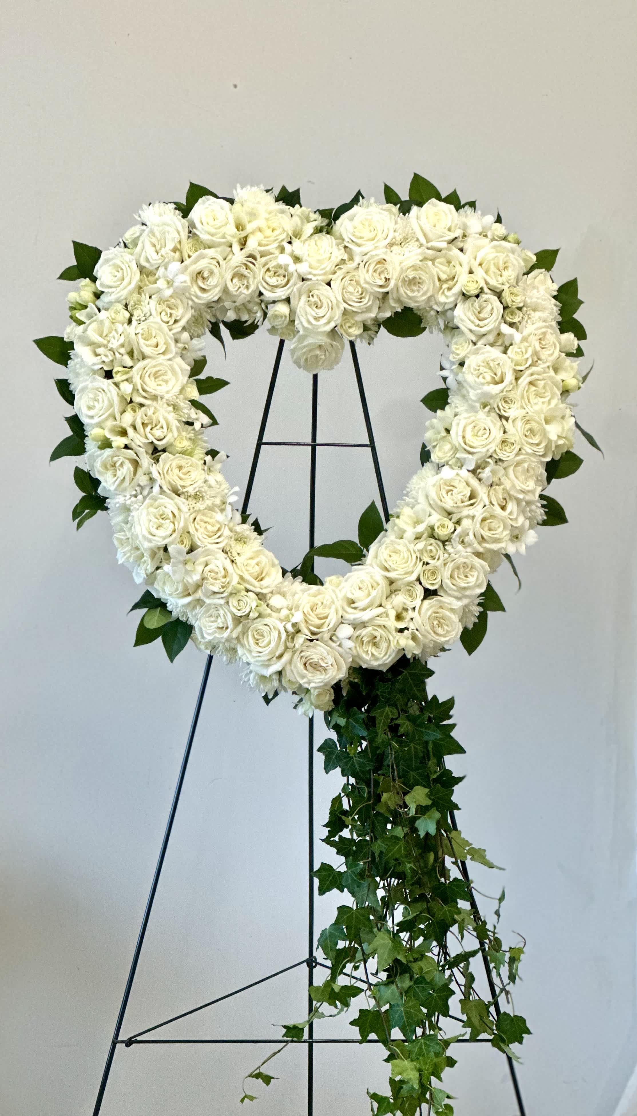 Heart-shaped white floral wreath on a stand with trailing ivy
