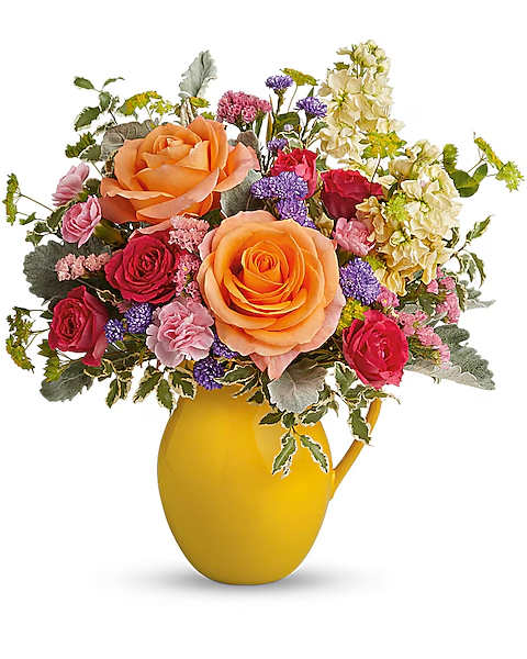 Mixed bouquet of roses and small flowers in a yellow pitcher vase
