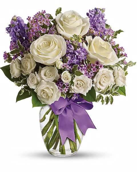 White roses and purple flowers arranged in a glass vase with a purple ribbon