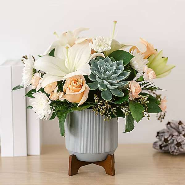 Arrangement of white lilies, peach roses, and a blue-green succulent in a ribbed vase