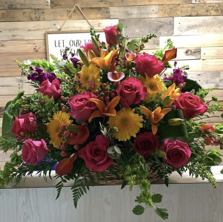 Mixed bouquet of pink roses, orange lilies, and yellow daisies in a basket