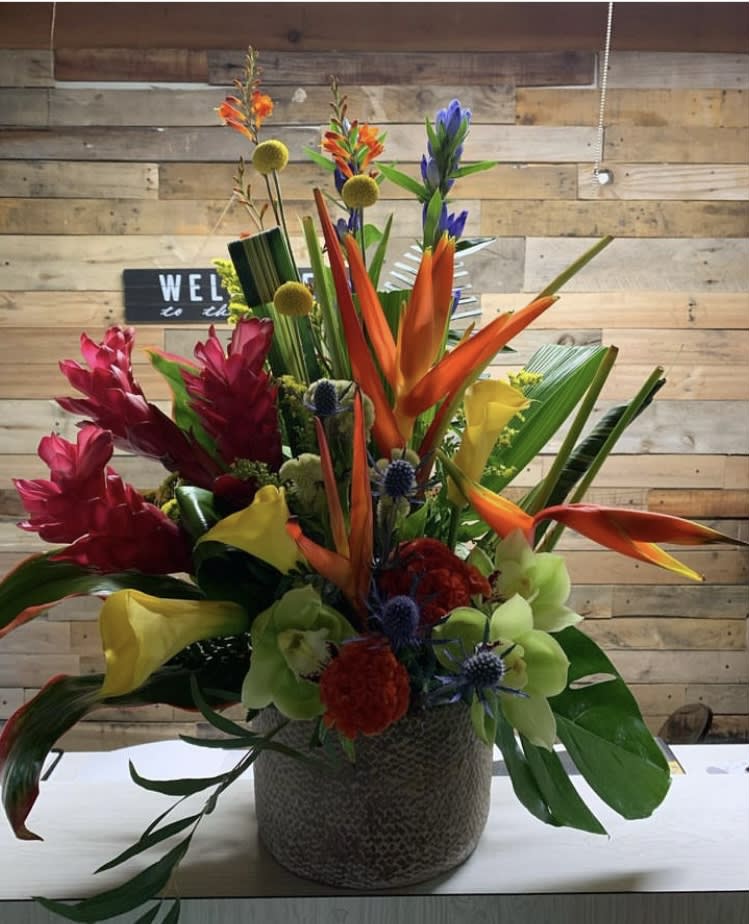 Tropical floral arrangement in a textured vase with orange, red, yellow, and green blooms